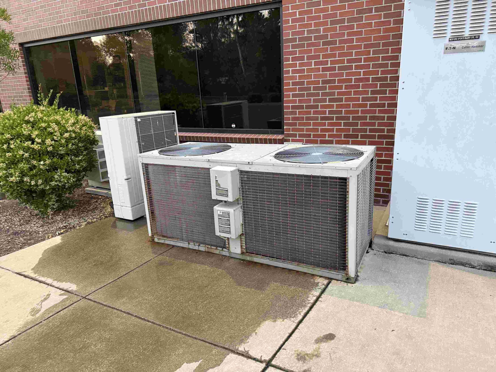 Large outdoor air conditioning unit next to a brick building.