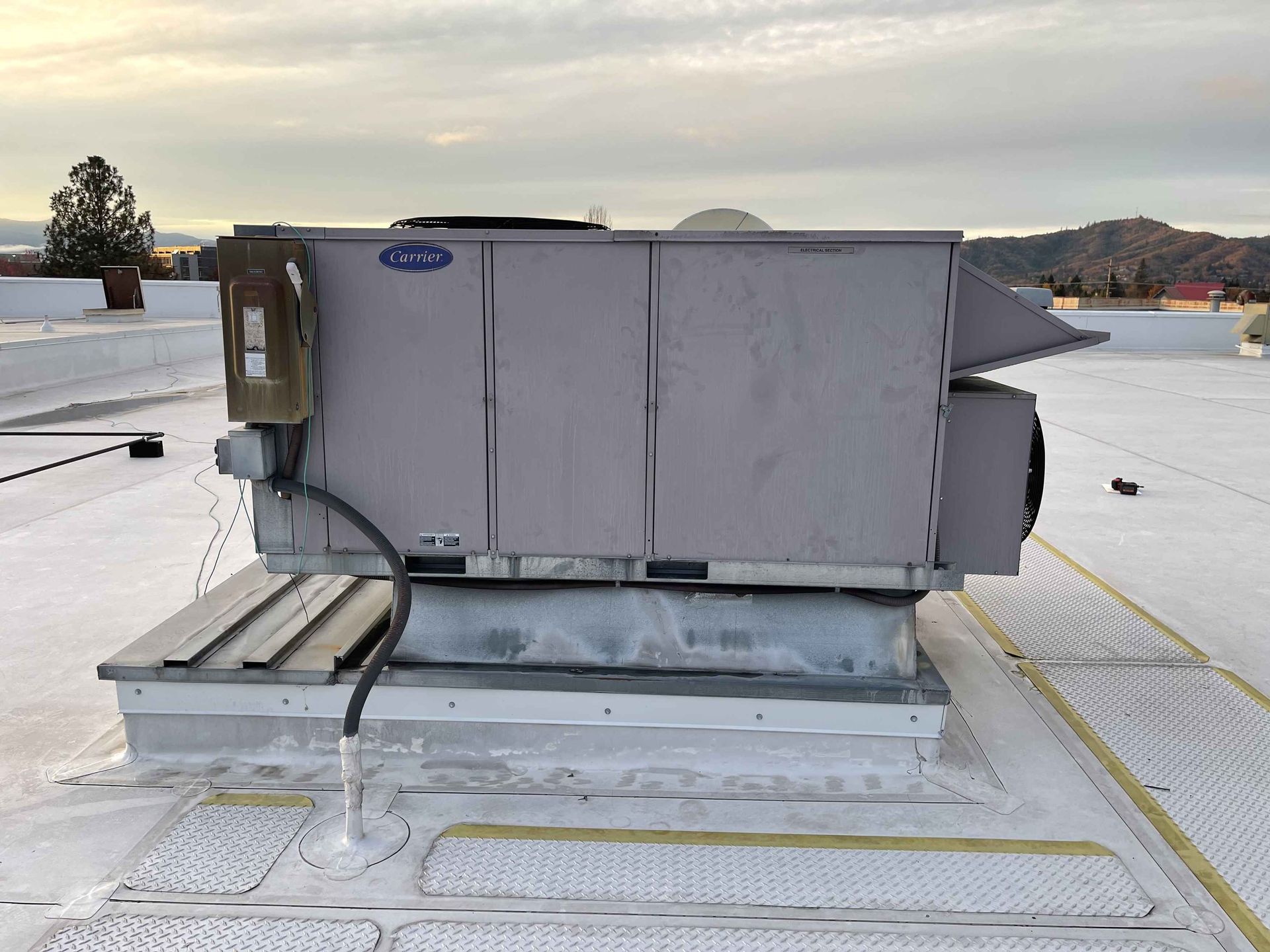Rooftop HVAC unit on a flat white roof against a cloudy sky.