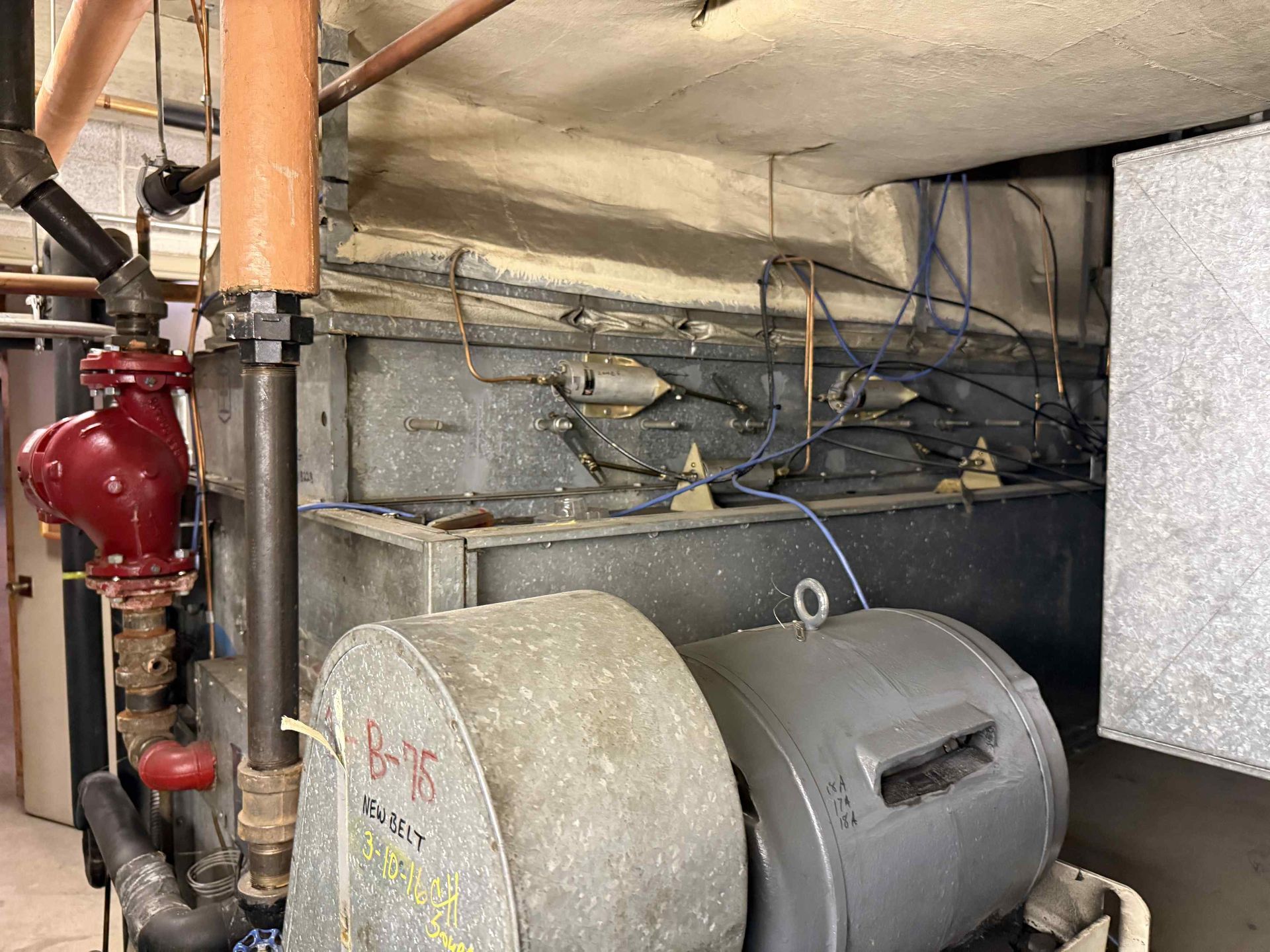 HVAC unit with pipes, valves, and a large blower in a mechanical room.