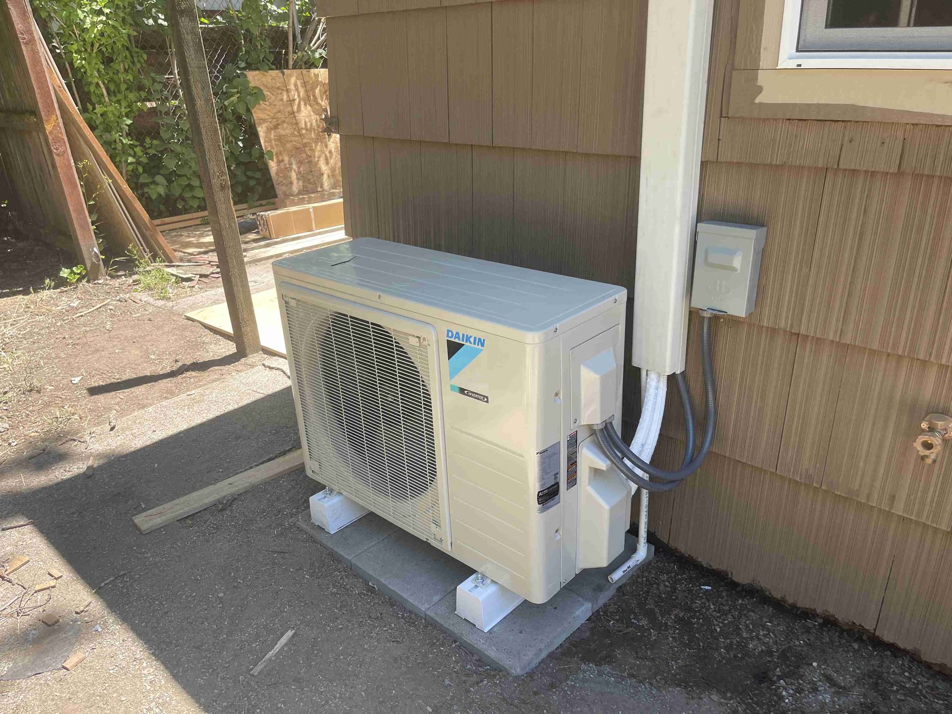 Outdoor air conditioning unit mounted on a concrete slab against a brown wall.