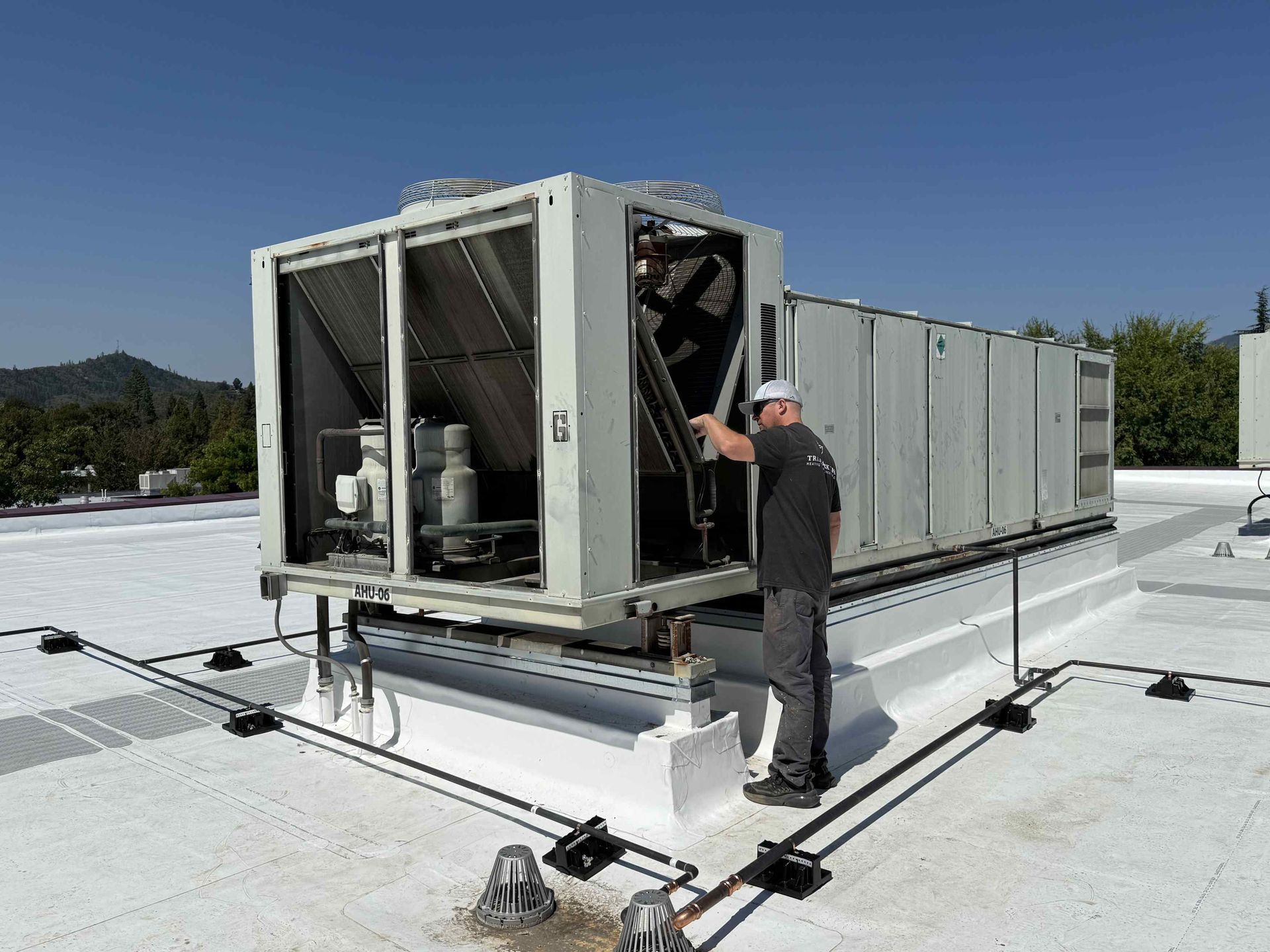 Man servicing HVAC unit on a white rooftop under a clear blue sky.