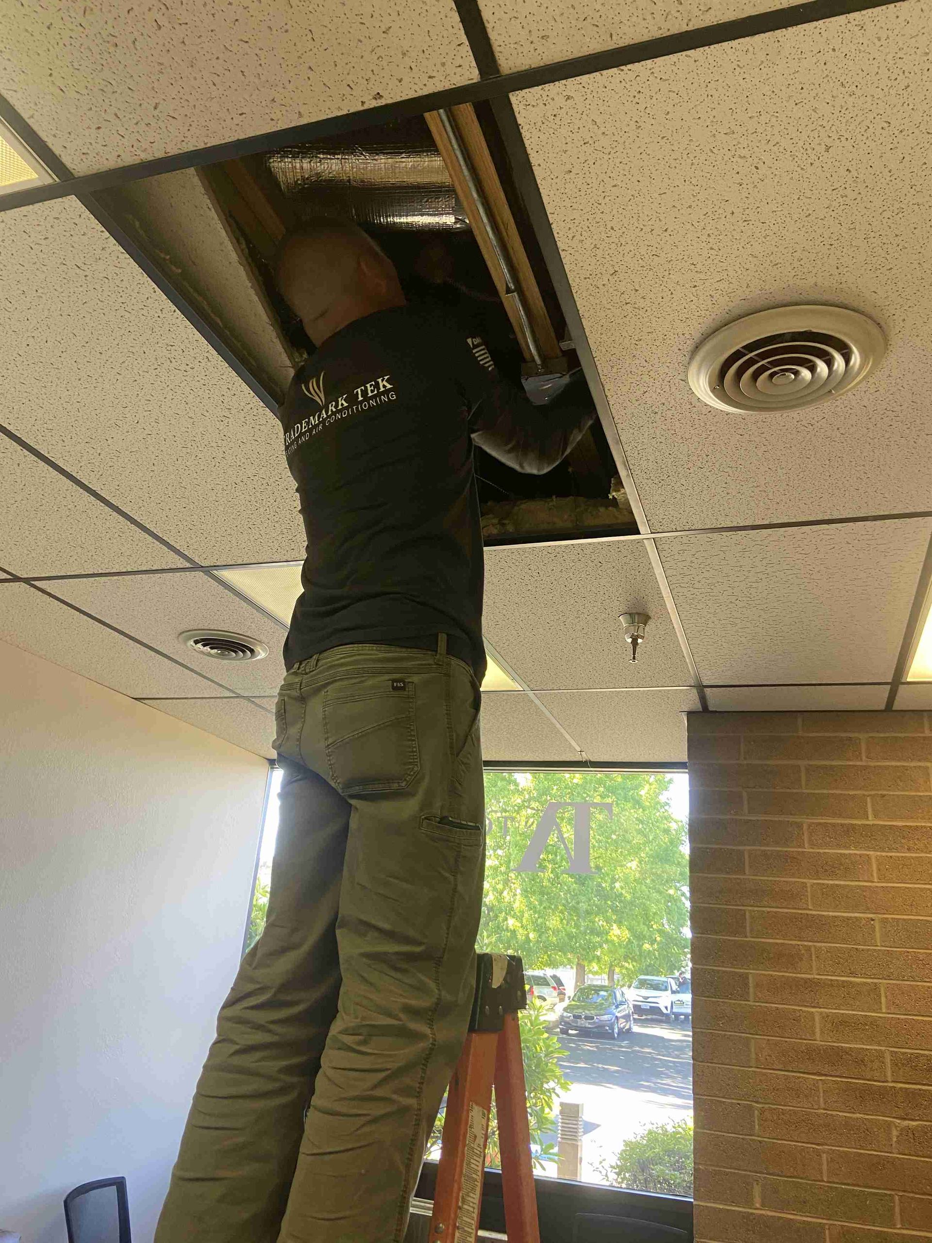 Man on a ladder installing a ceiling panel in an office.
