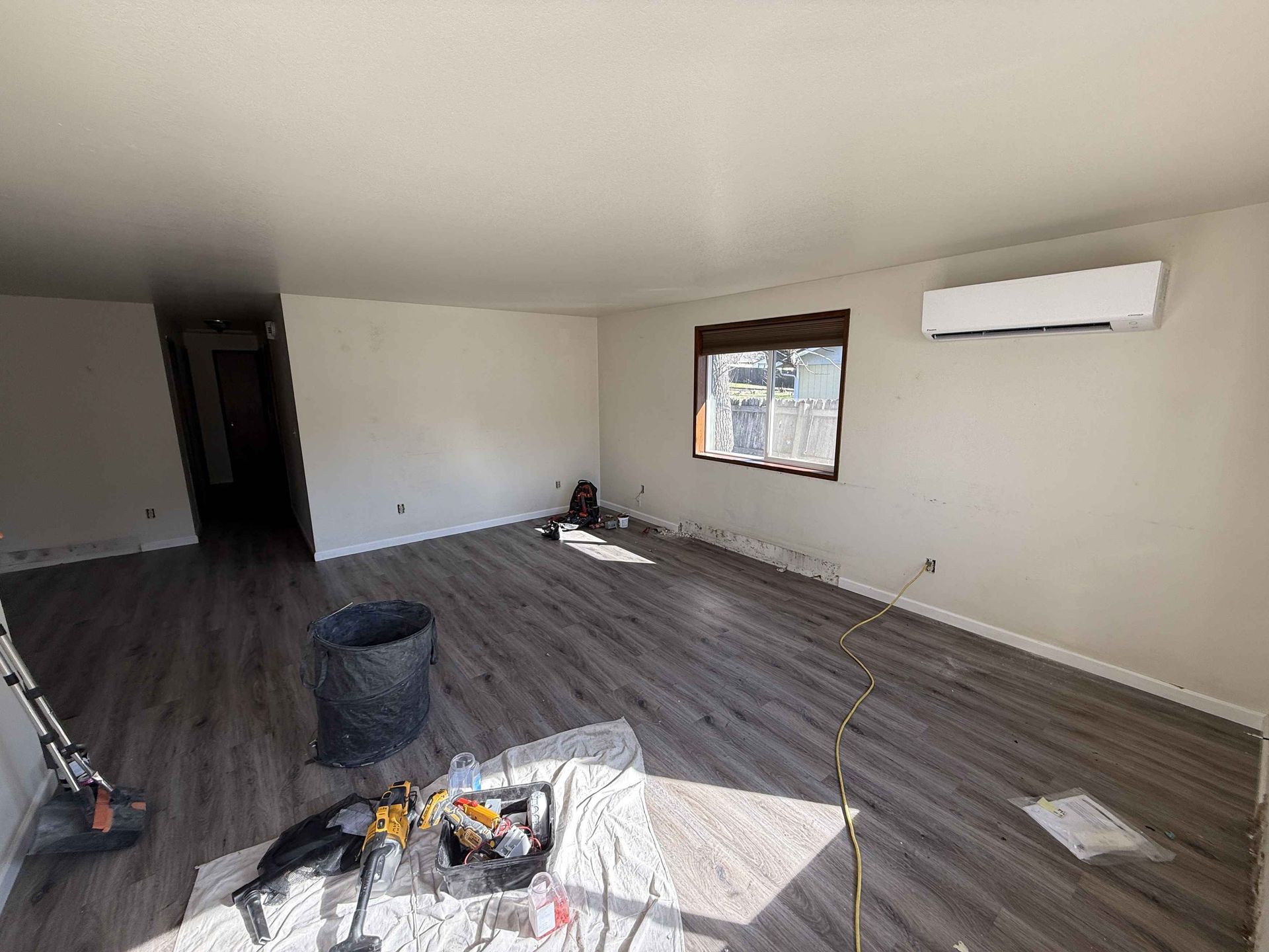 Empty living room with wood-look flooring, white walls, and an air conditioning unit.