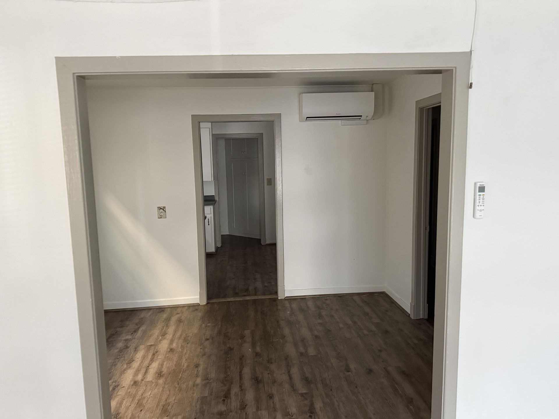 Interior view of an apartment with wood floors, gray trim, and an air conditioning unit.