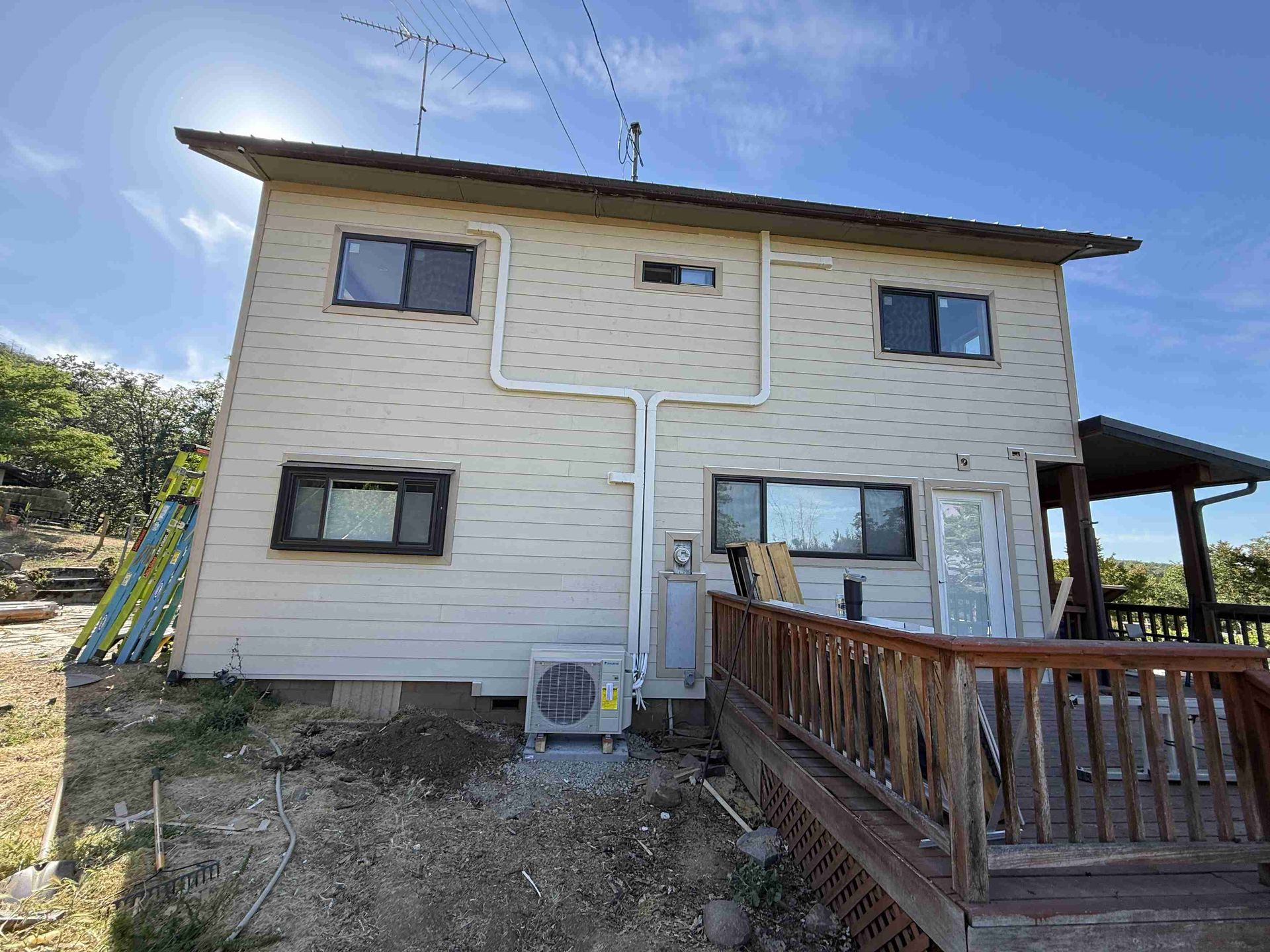 Two-story house with light beige siding, dark-framed windows, and a wooden deck.