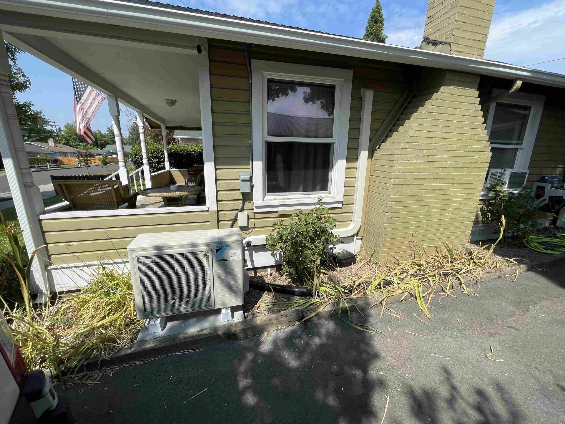 Exterior of a green house with a porch and air conditioning unit.