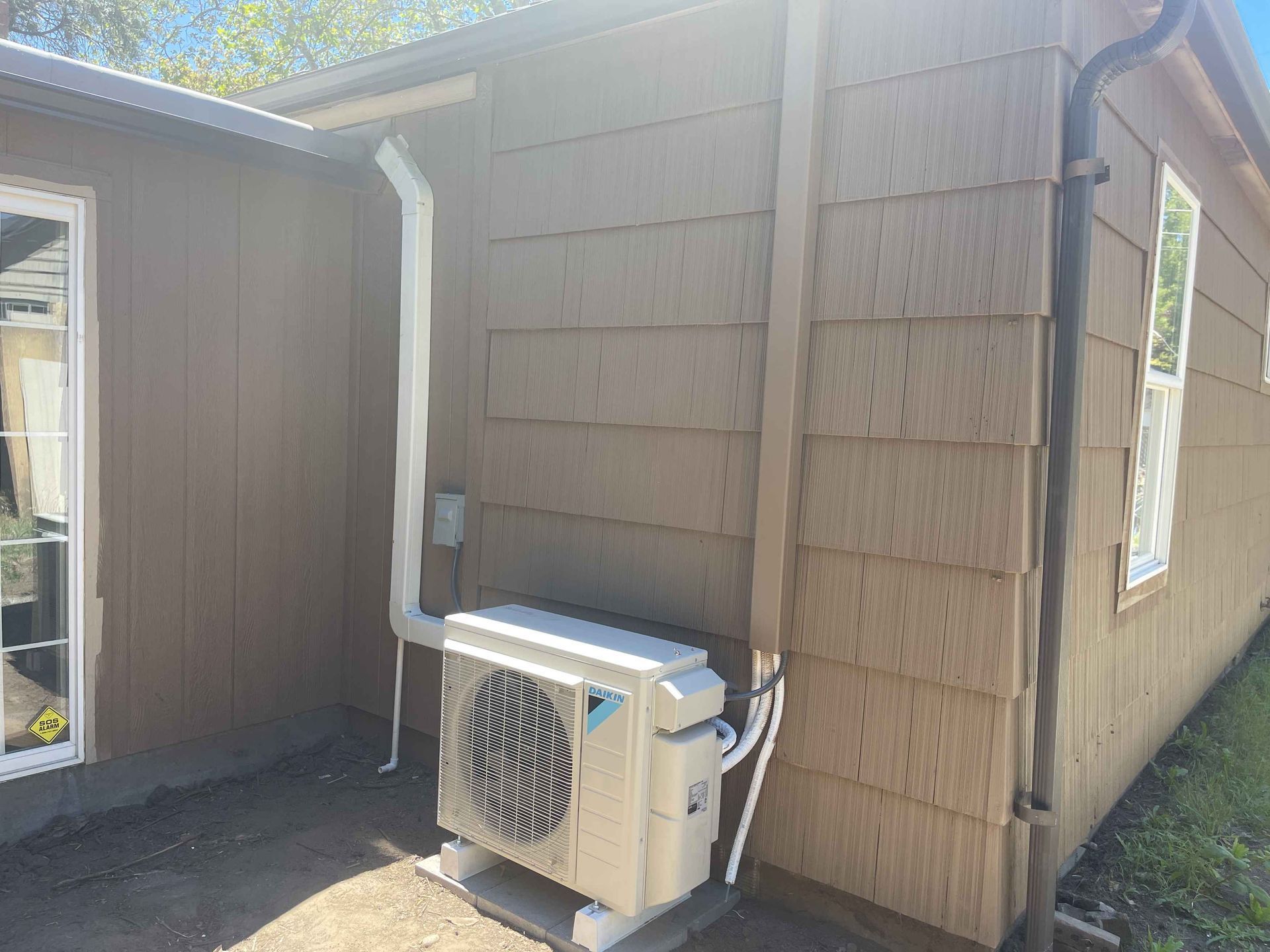 An air conditioning unit is installed on a concrete pad outside a brown house.
