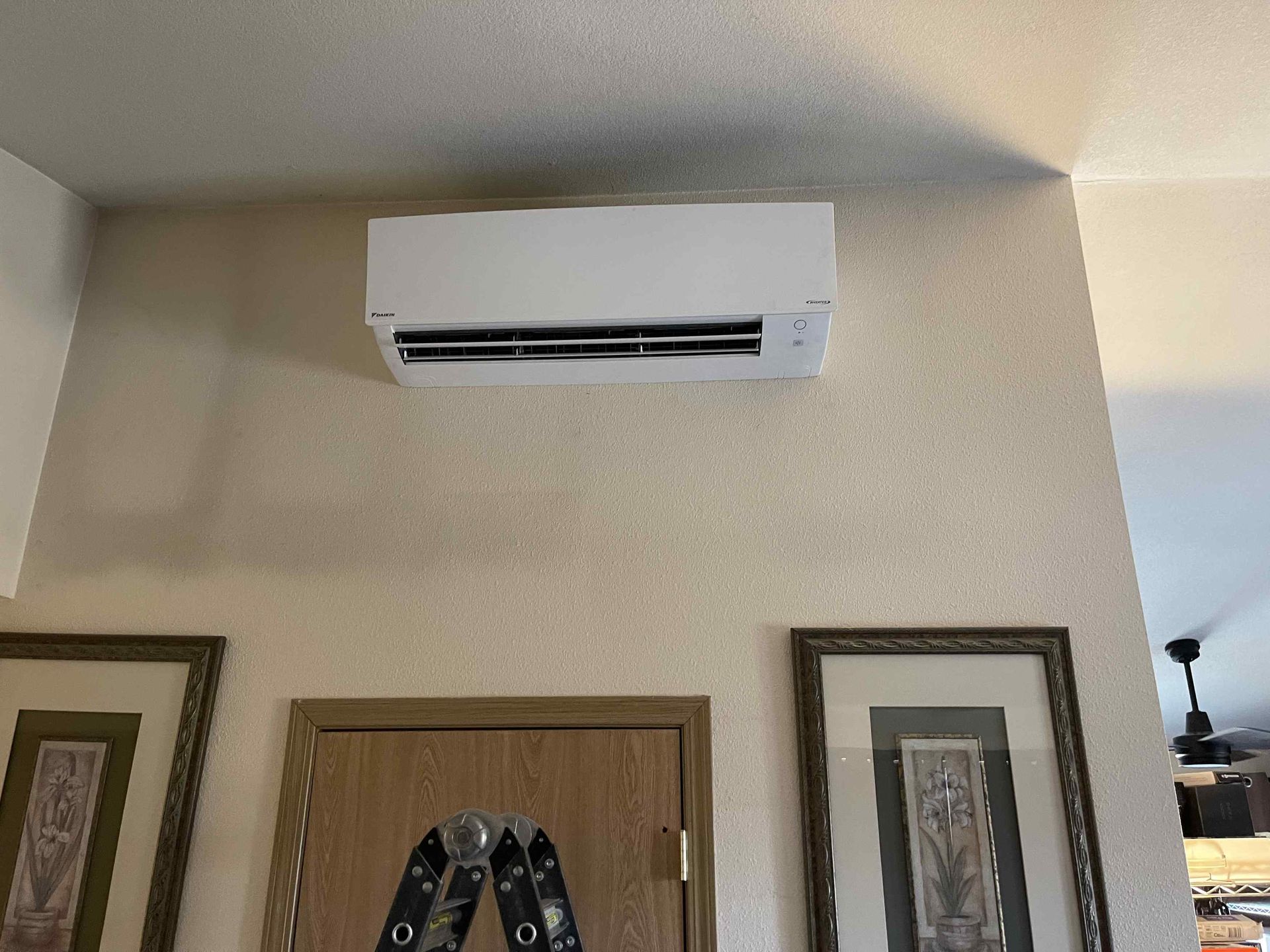 White ductless AC unit on a textured wall above a door and framed pictures.