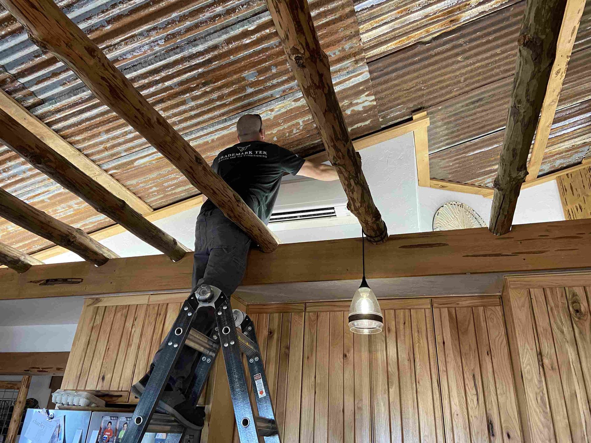 Person on ladder installing something on a wood beam ceiling with a corrugated metal roof.