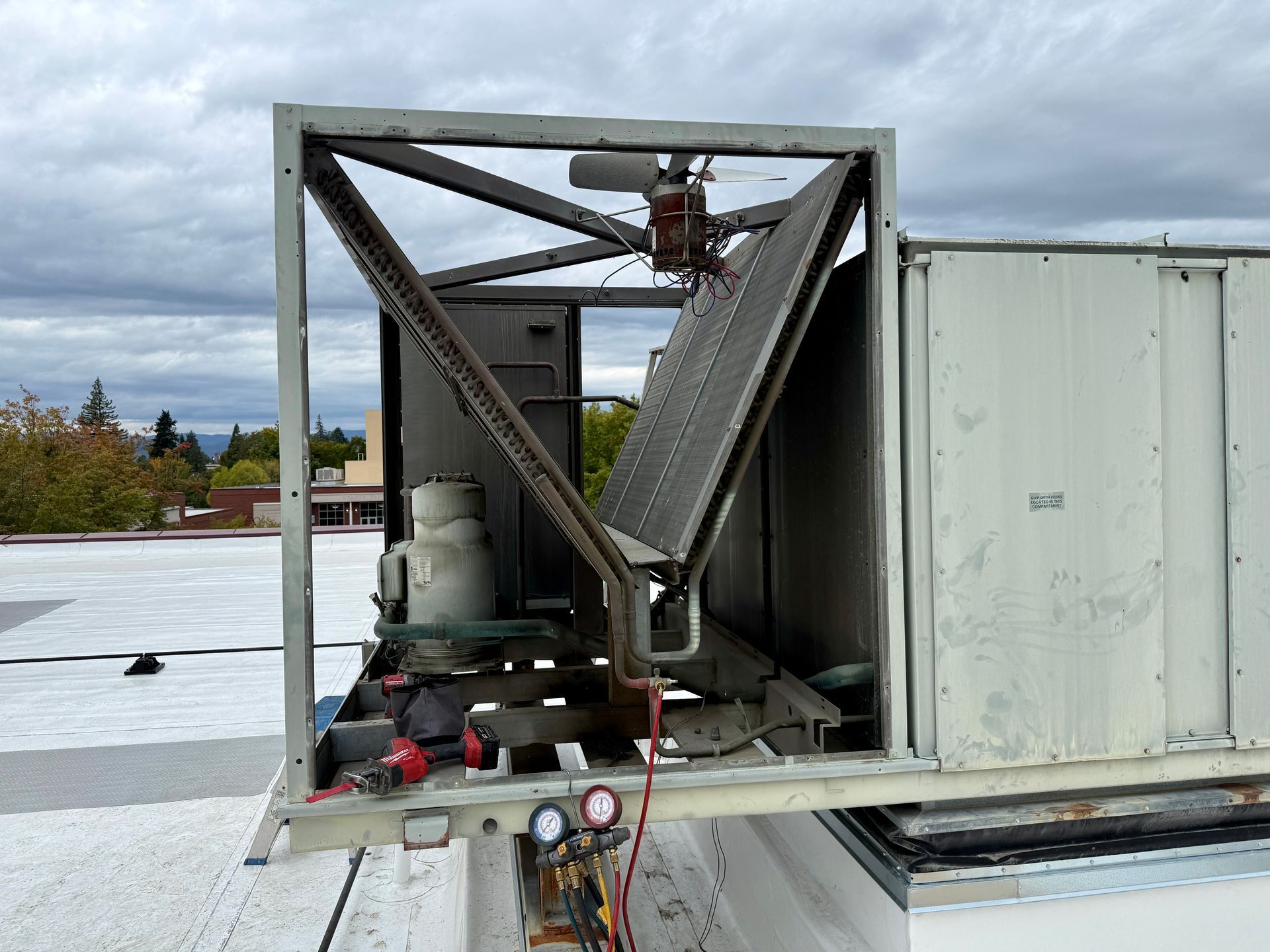 HVAC unit on a rooftop being serviced. Shows open metal framework, coils, and gauges.