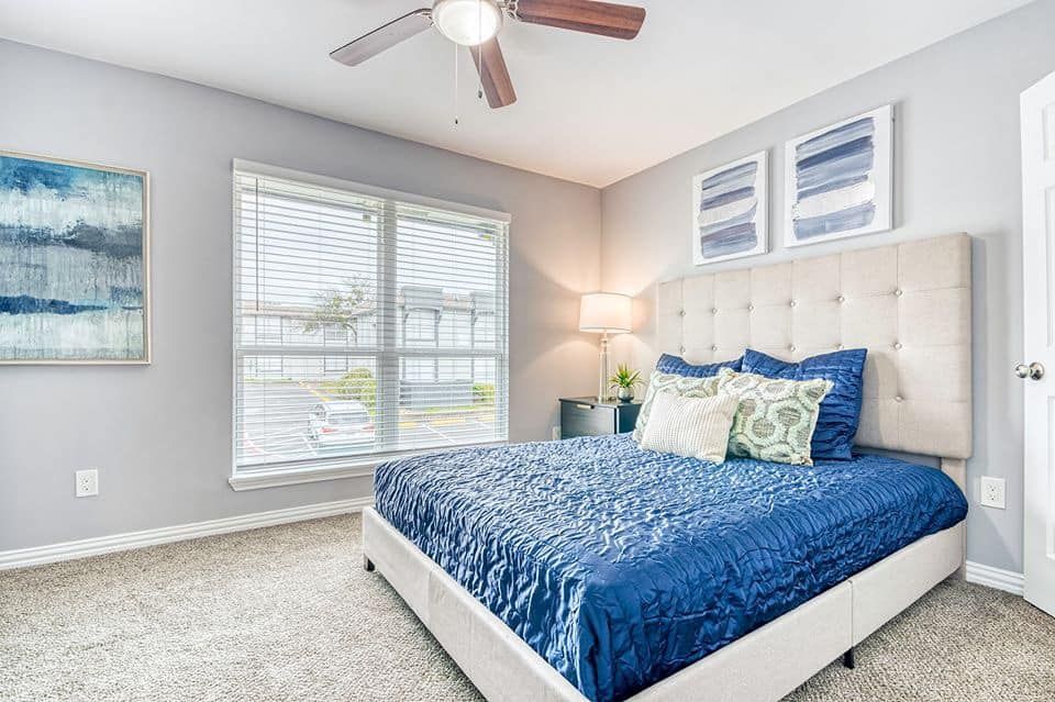 Bedroom with blue bedding, window, and neutral decor.