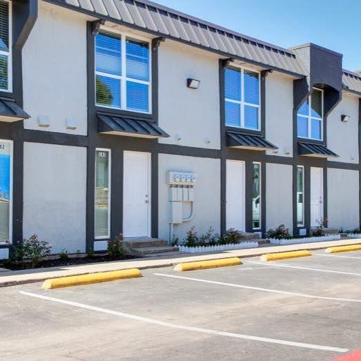 Row of townhouses with white walls, dark trim, windows, and parking spaces.