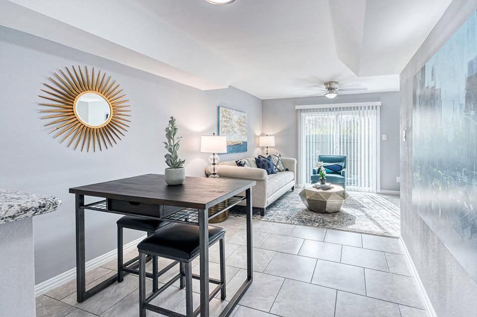 Dining area with table, sunburst mirror, and open to a living room with sofa and outdoor view.