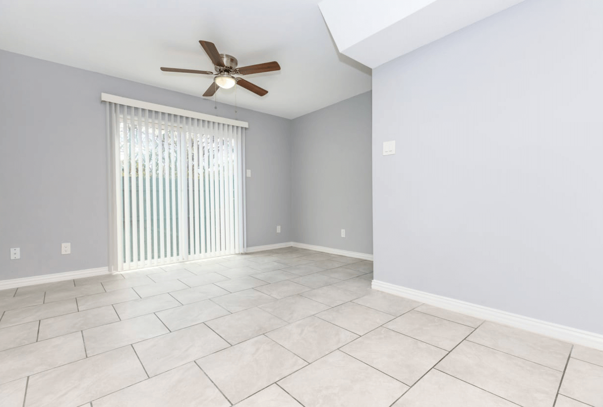 Empty room with gray walls, sliding glass door, tiled floor, and ceiling fan.
