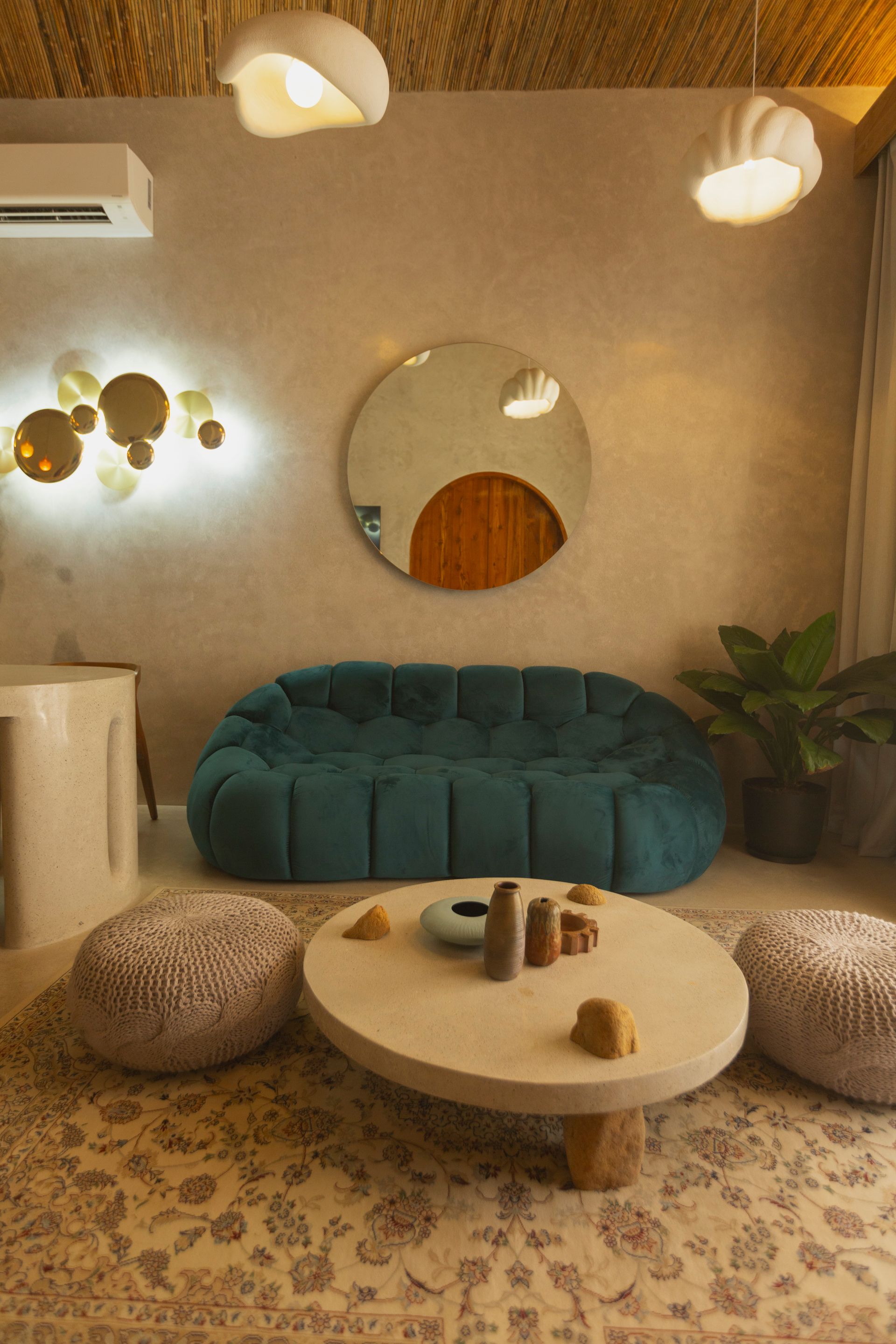 Living room with teal sofa, round table, poufs, and a decorative wall mirror.