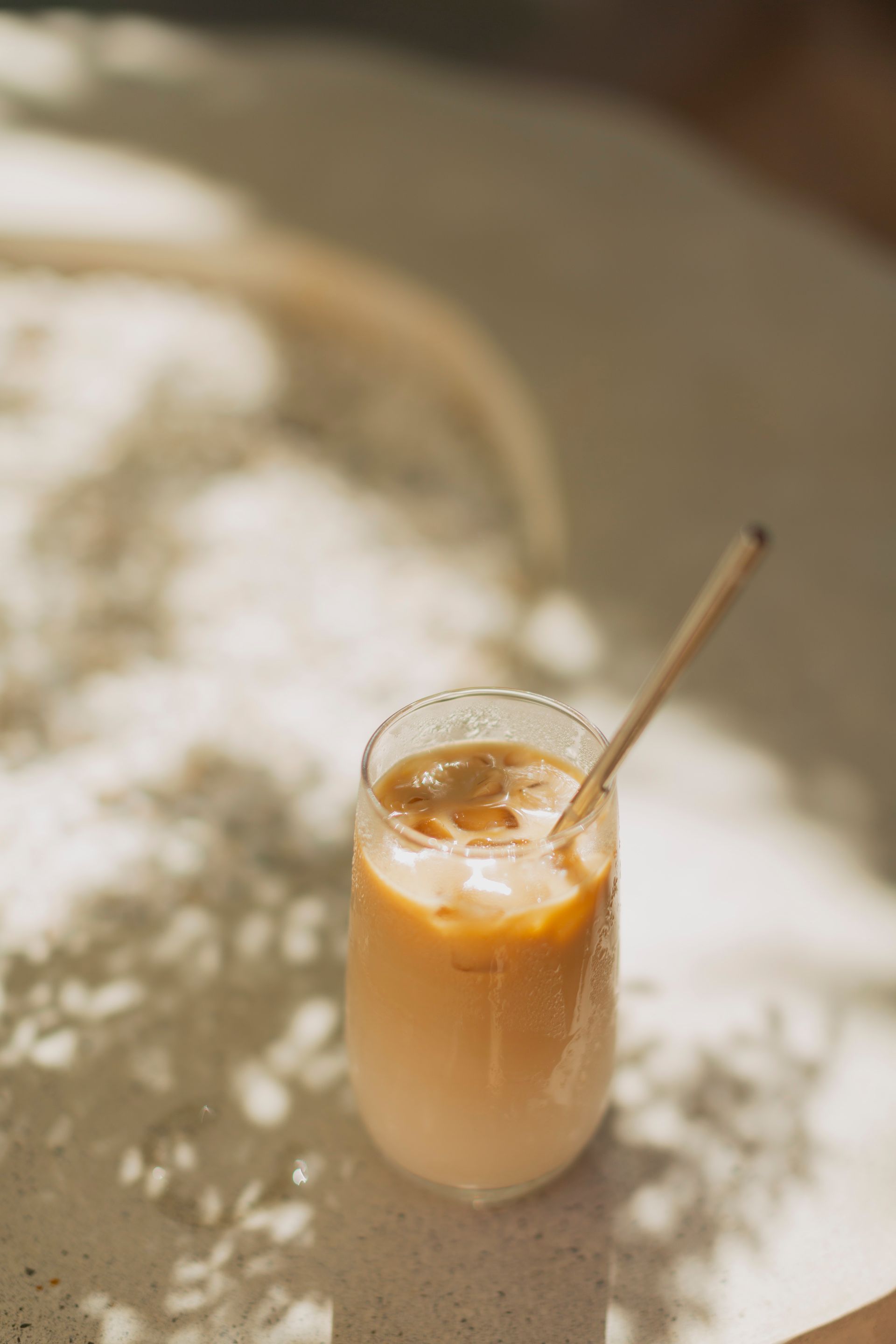 Iced coffee in a clear glass with a straw, casting shadows on a white surface.