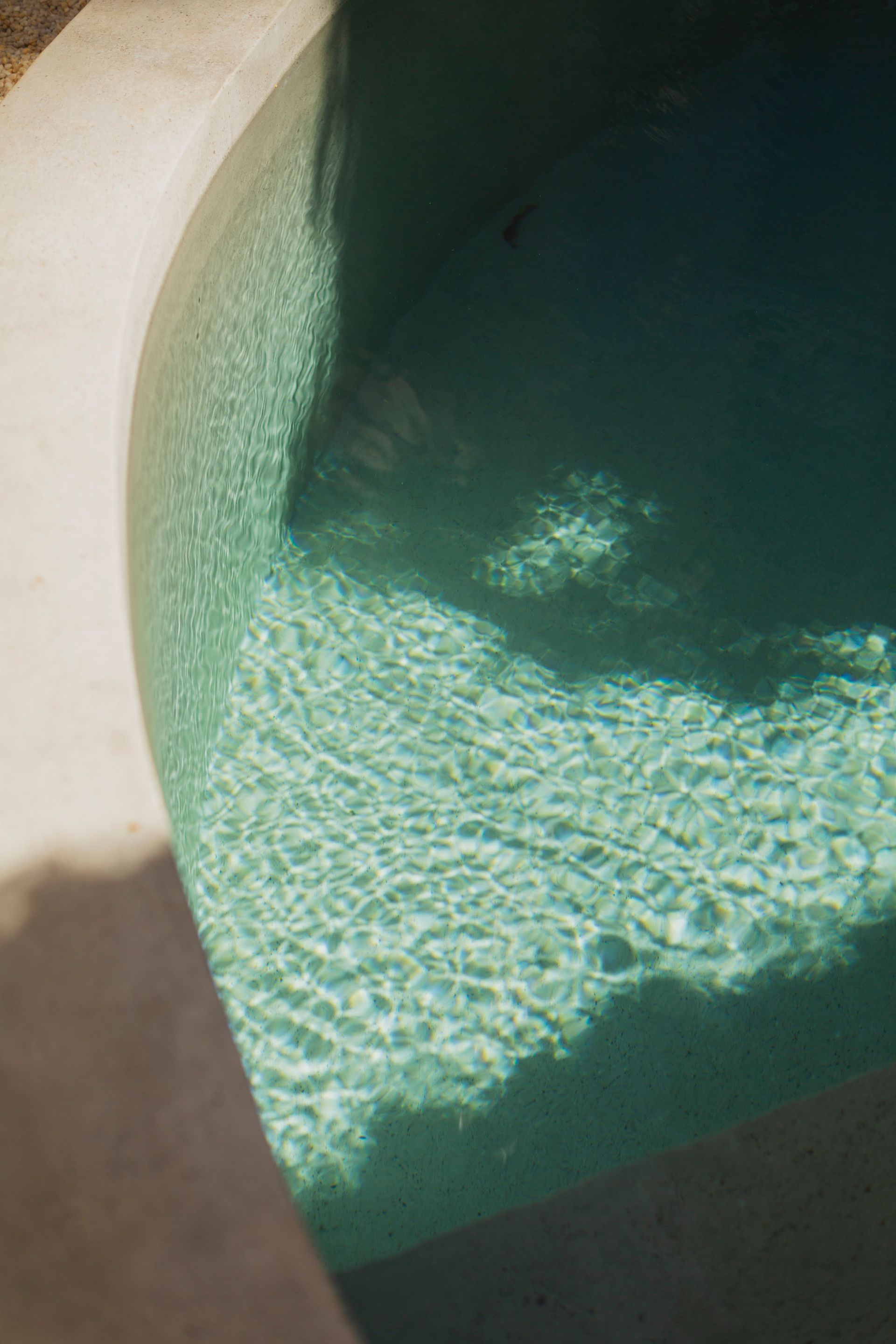 Curved turquoise pool with a white concrete edge; shadows create contrast.