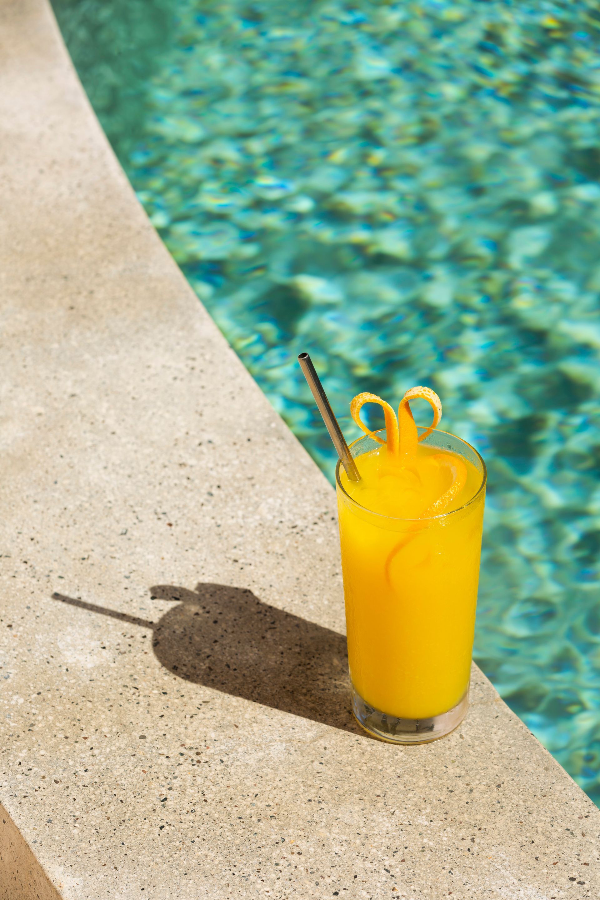 Yellow drink with straw, next to a pool.