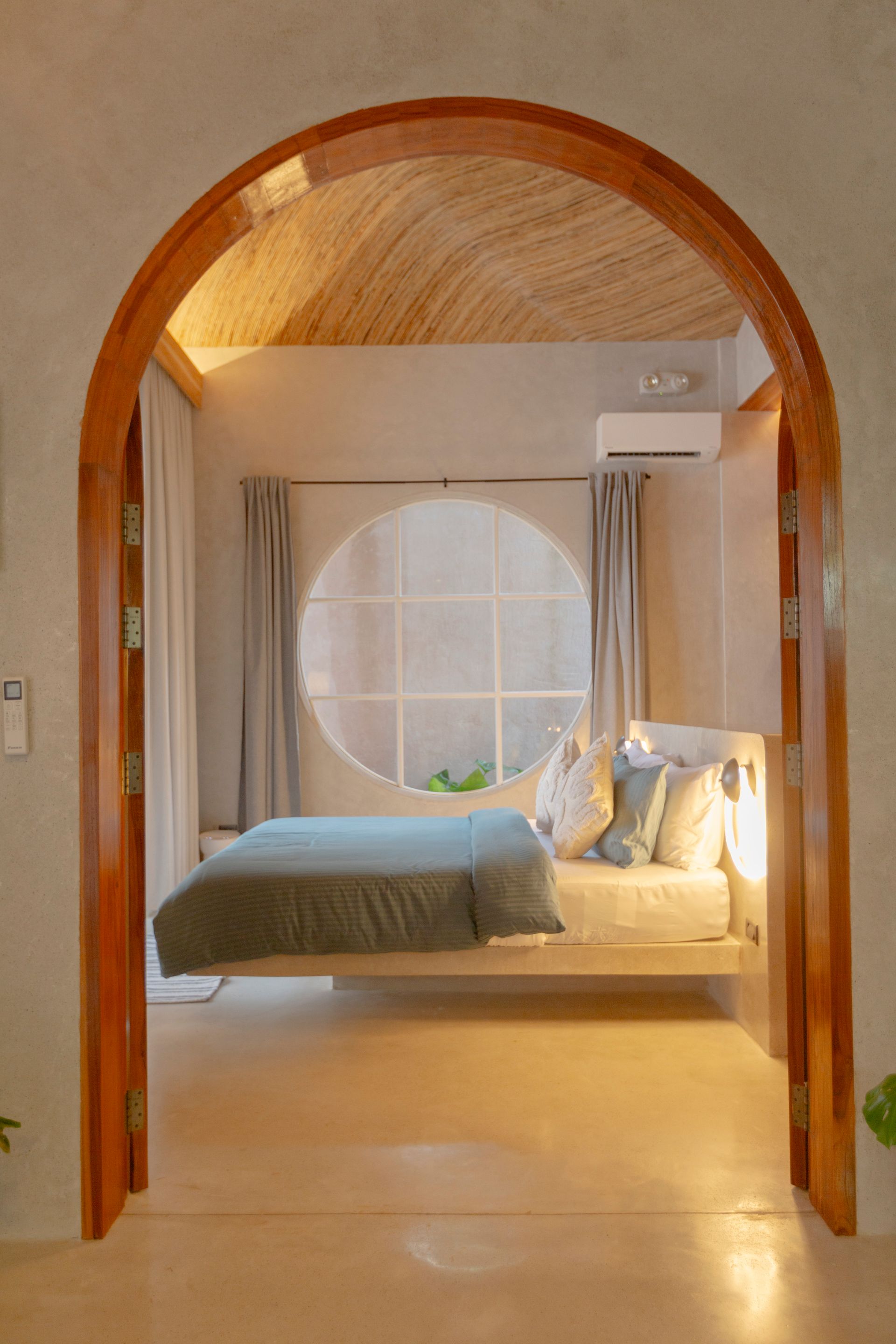Bedroom interior with arched wooden doorway, circular window, bed with blue bedding, and neutral color scheme.