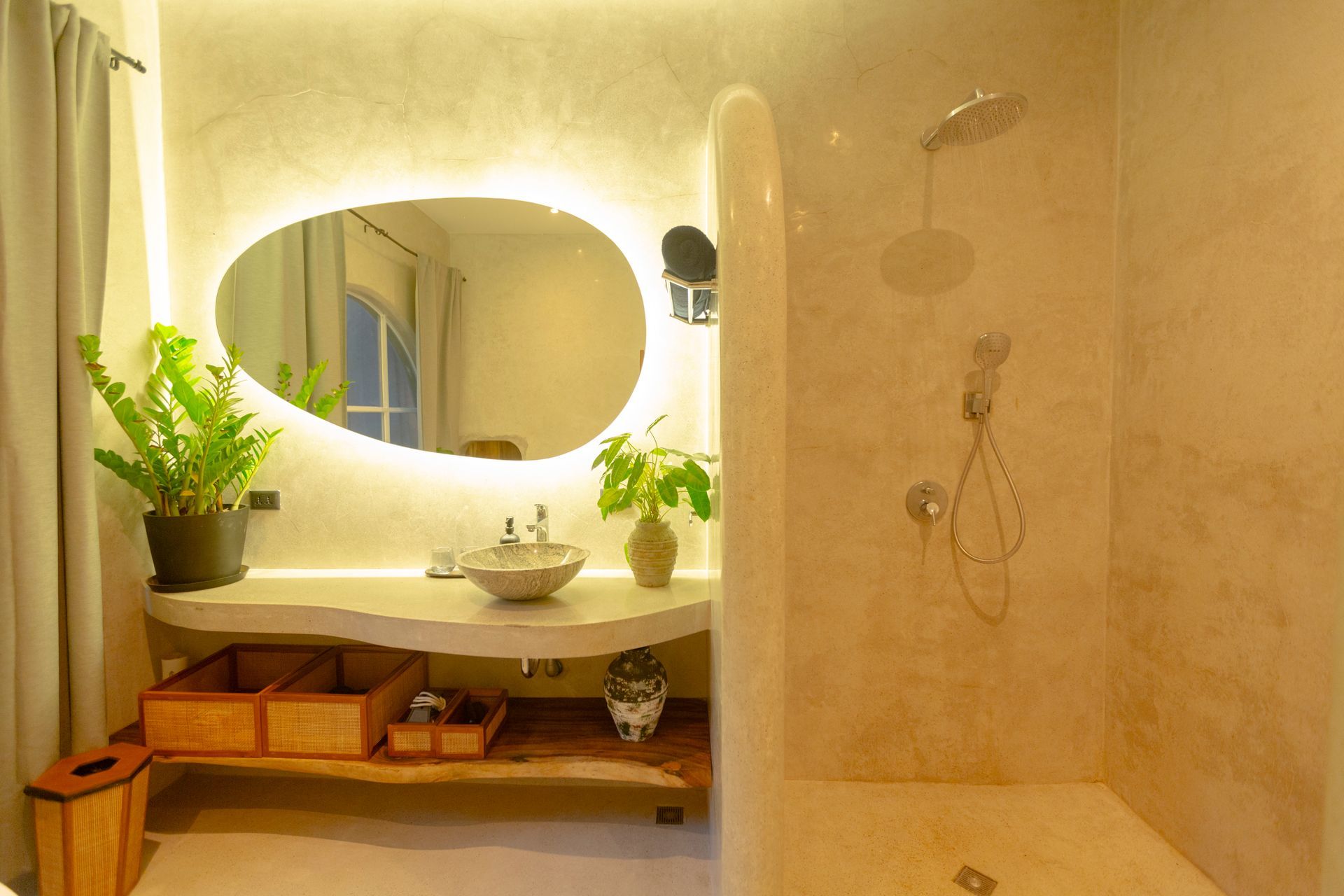 Bathroom with an irregularly shaped mirror, illuminated, and a walk-in shower. Natural light and plants are present.