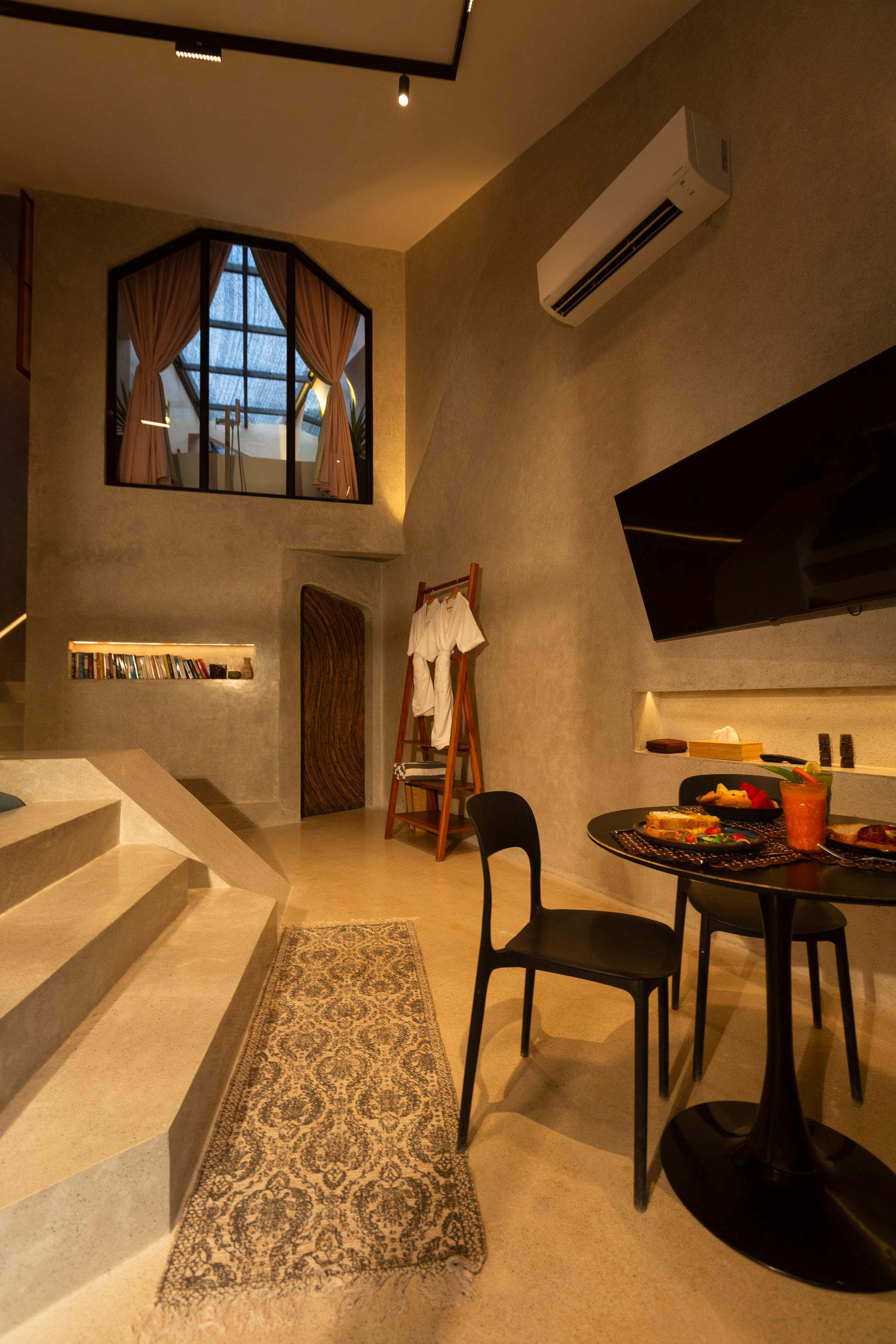 Interior with stairs, round table, black chairs, and a large window with pink curtains.