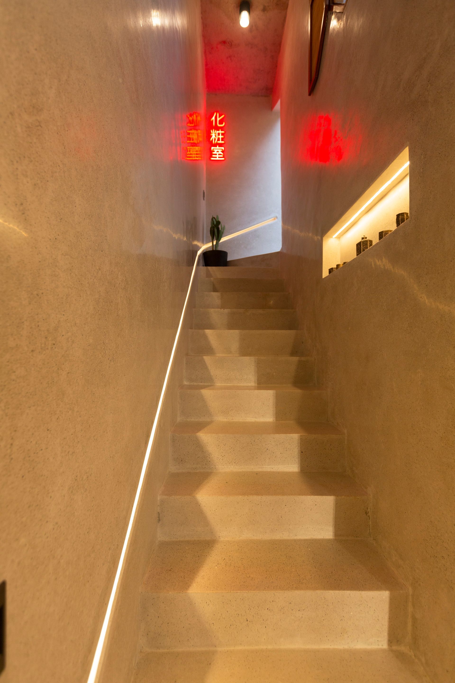Staircase with light-colored speckled walls and steps, leading up. Red neon signs are visible near the top.