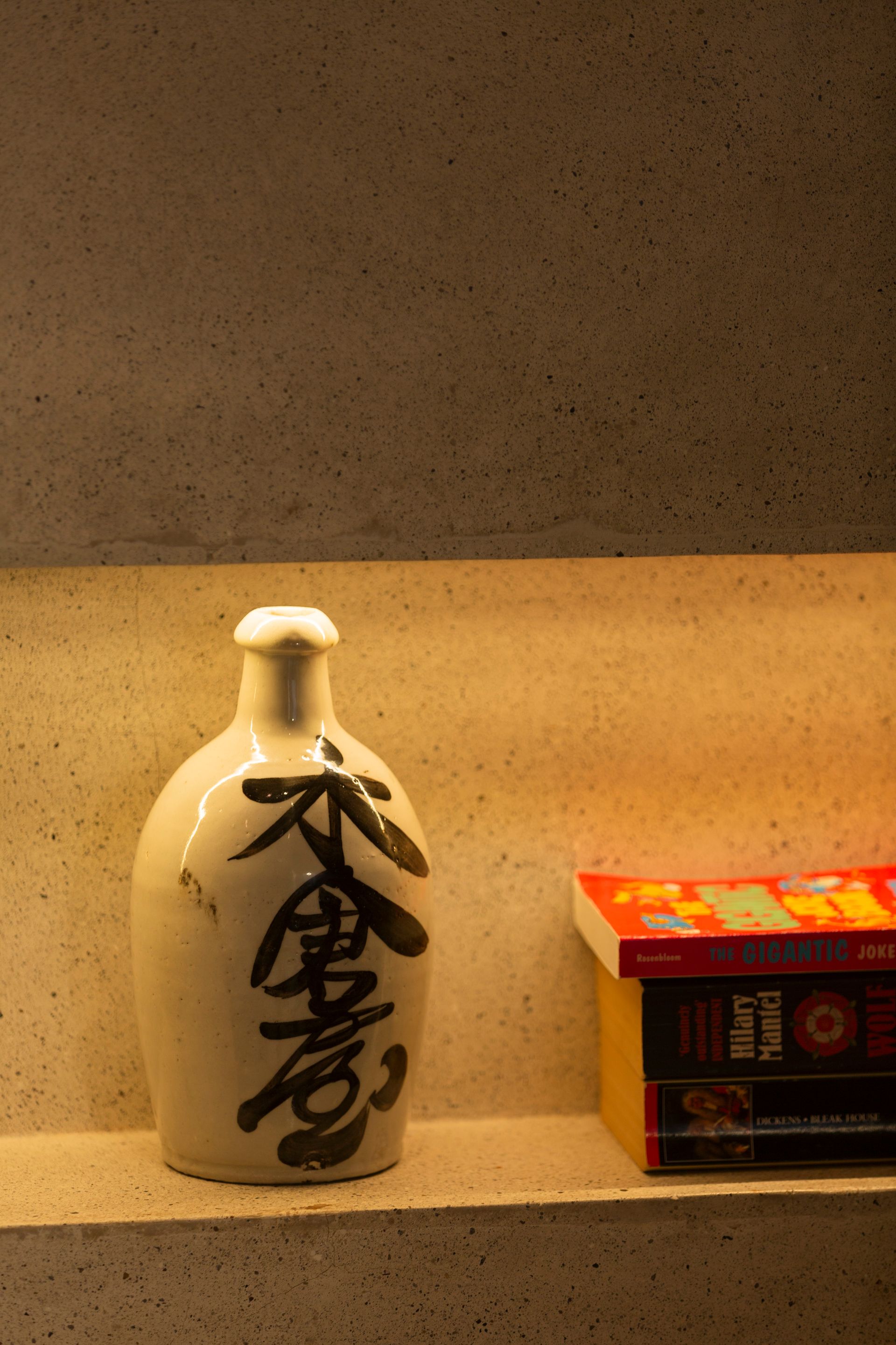 Ceramic sake bottle with black script, next to stacked red and black books on a shelf.