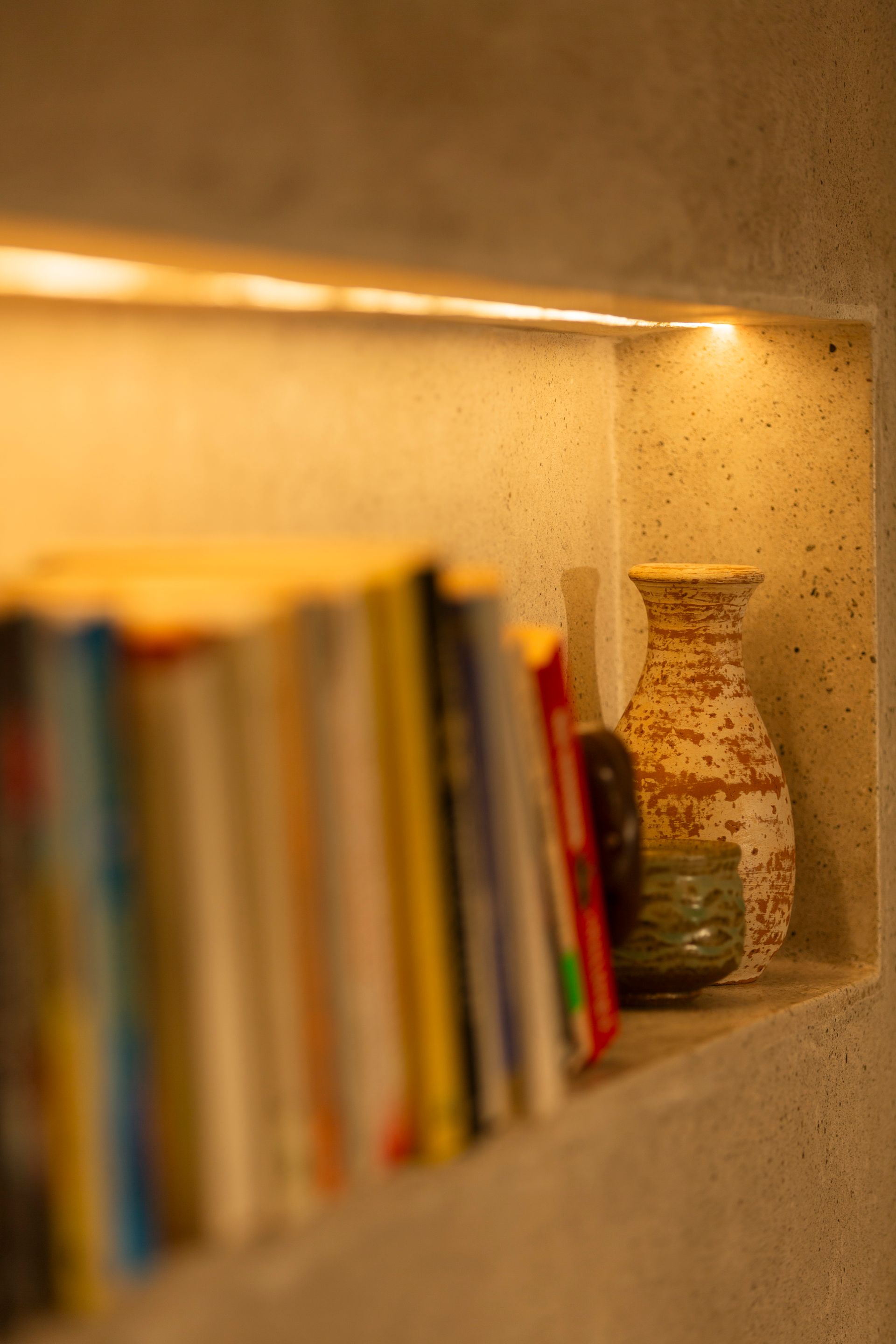 Books and pottery displayed on a shelf in a recessed, lit space.