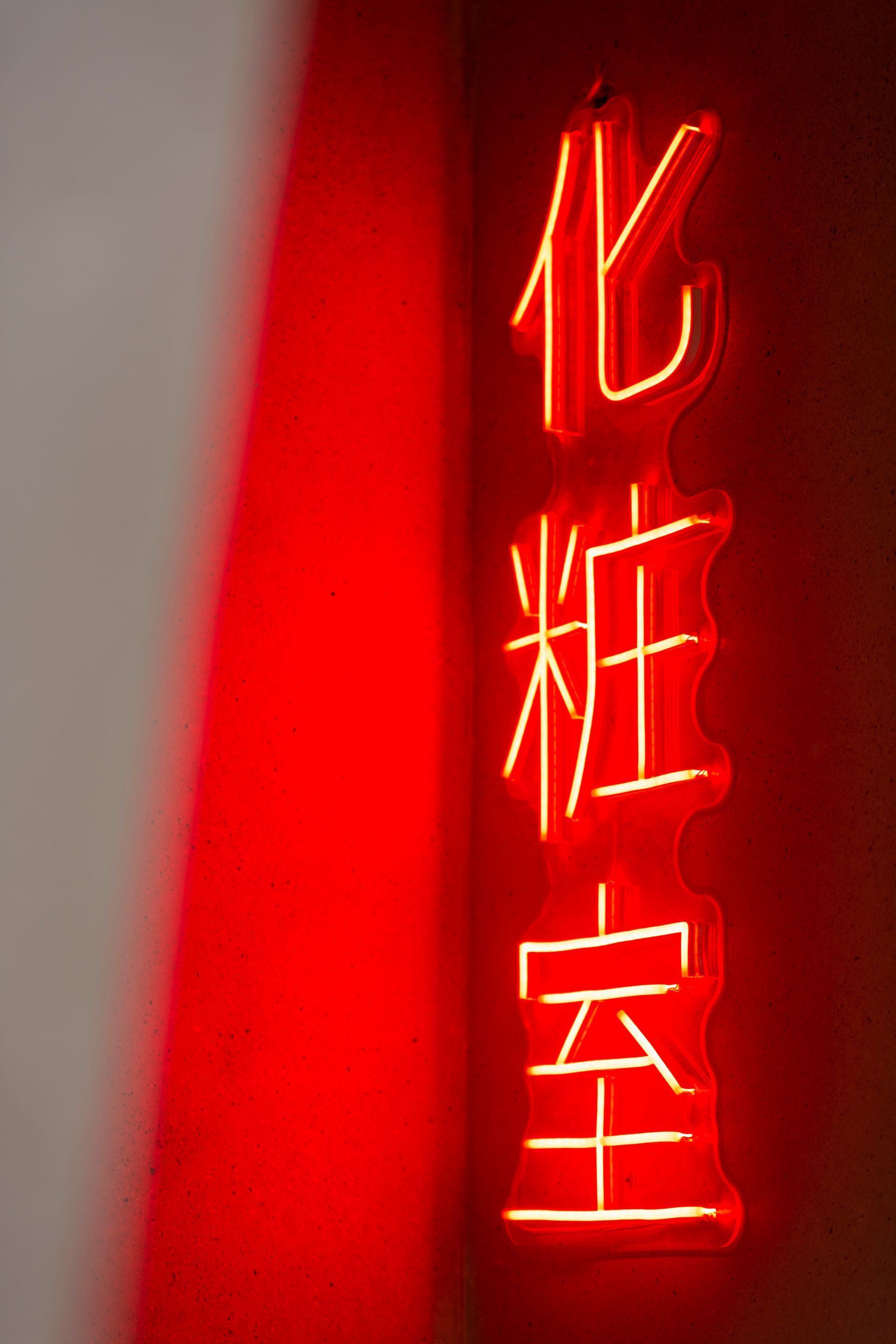 Red neon sign with vertical Chinese characters, on a dark brown wall.