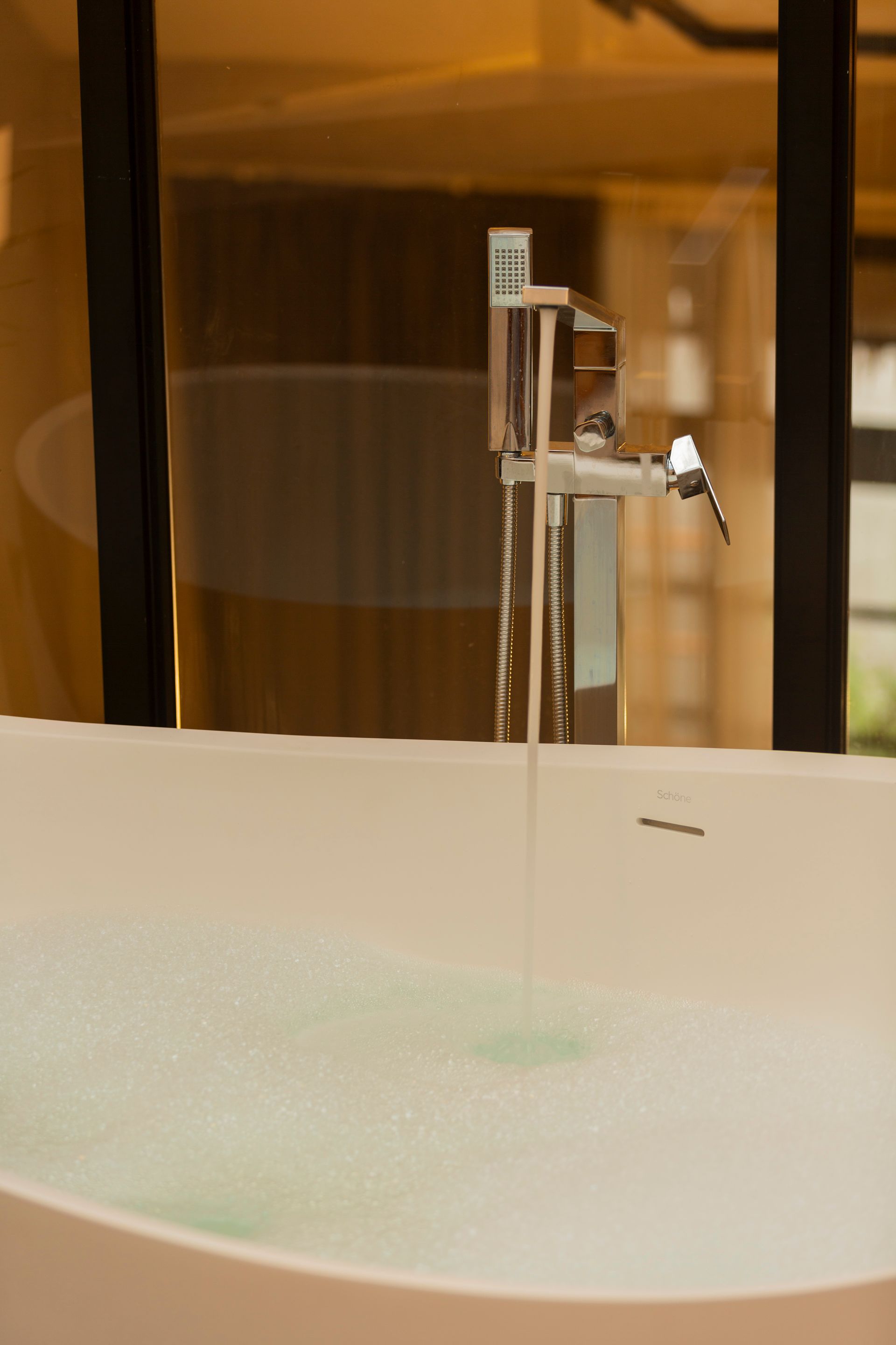 Bathtub filling with water from a tall, modern faucet.