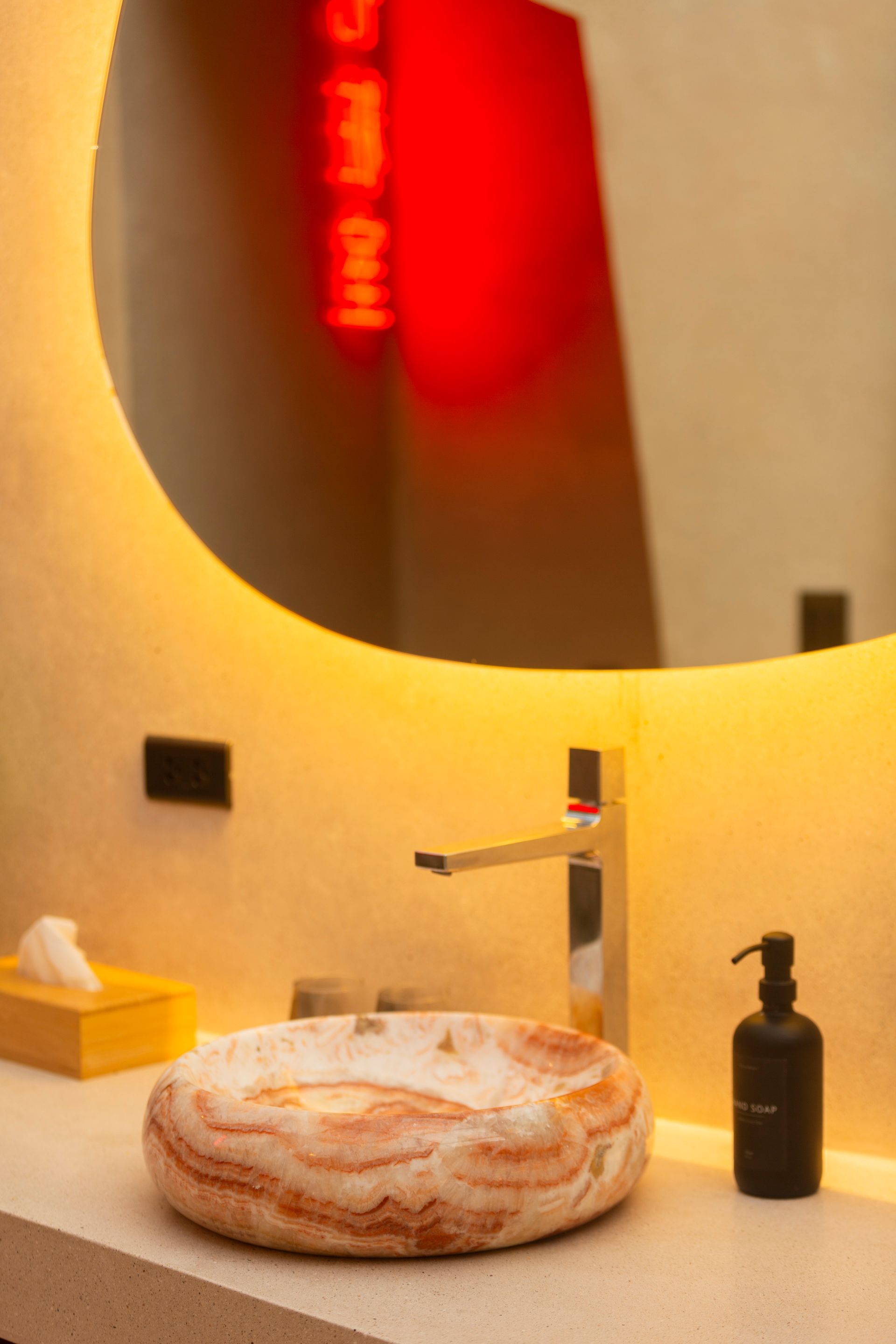 Bathroom with a marble sink, illuminated mirror, and a black soap dispenser.