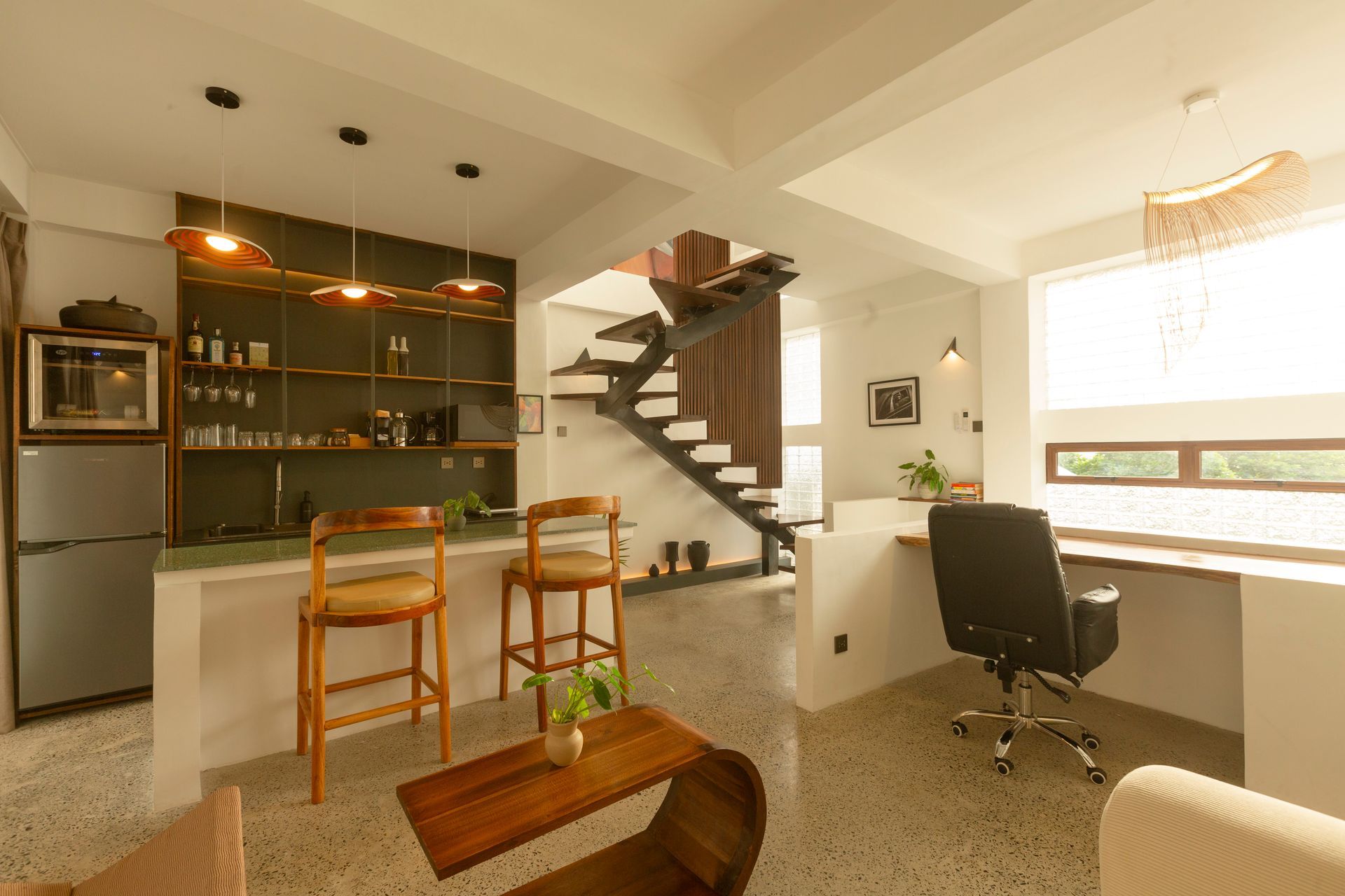 Modern open-concept living space with kitchen, dining area, desk, and staircase. Features wood and white accents.