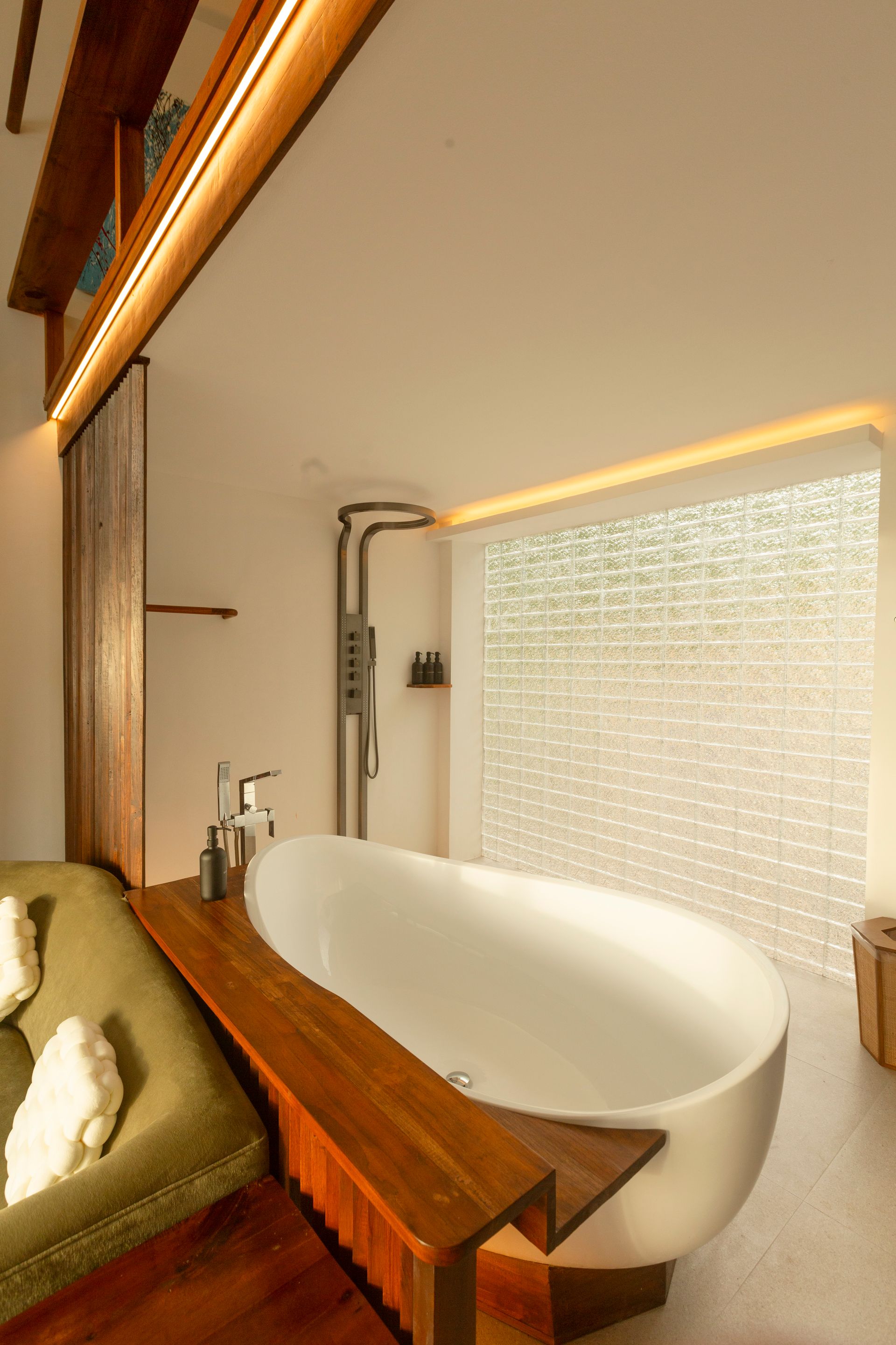 White oval bathtub in a modern bathroom with wood accents, shower, and frosted glass wall.