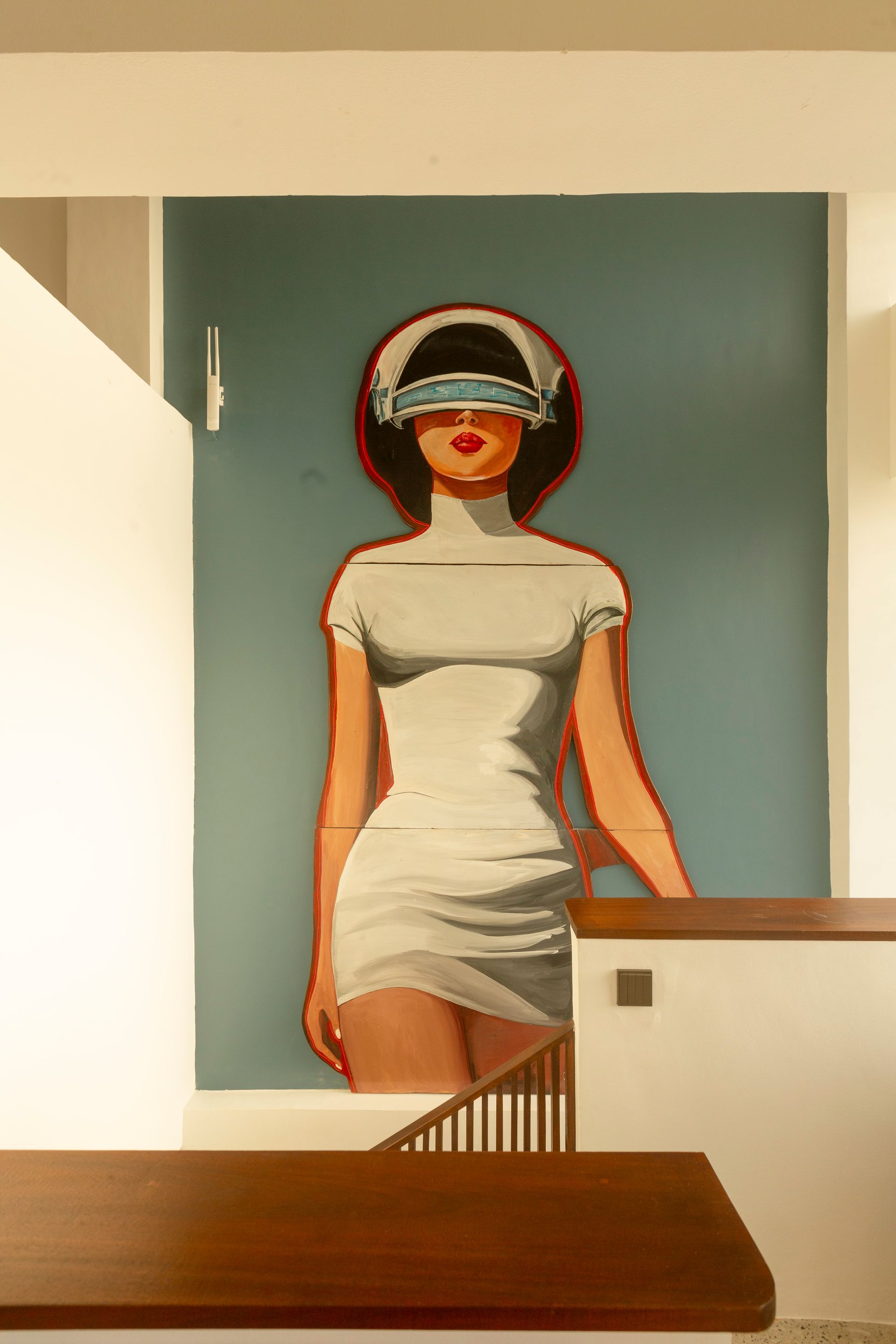 Mural of a woman in a white dress and blindfold-like headgear, standing against a teal background.
