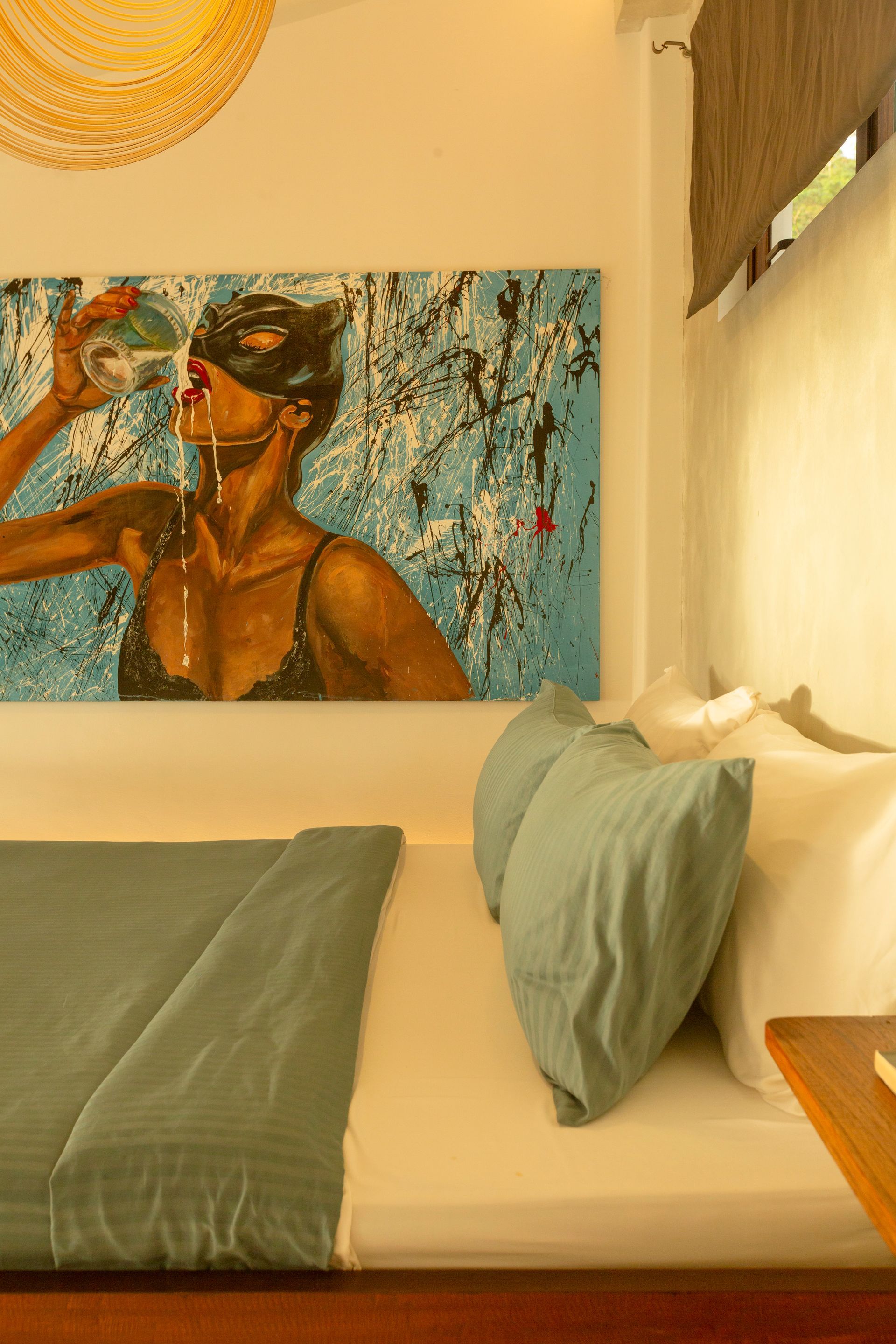 Bedroom interior with art, bed, and pillows. Light blue bed cover and pillows, artwork of woman drinking.