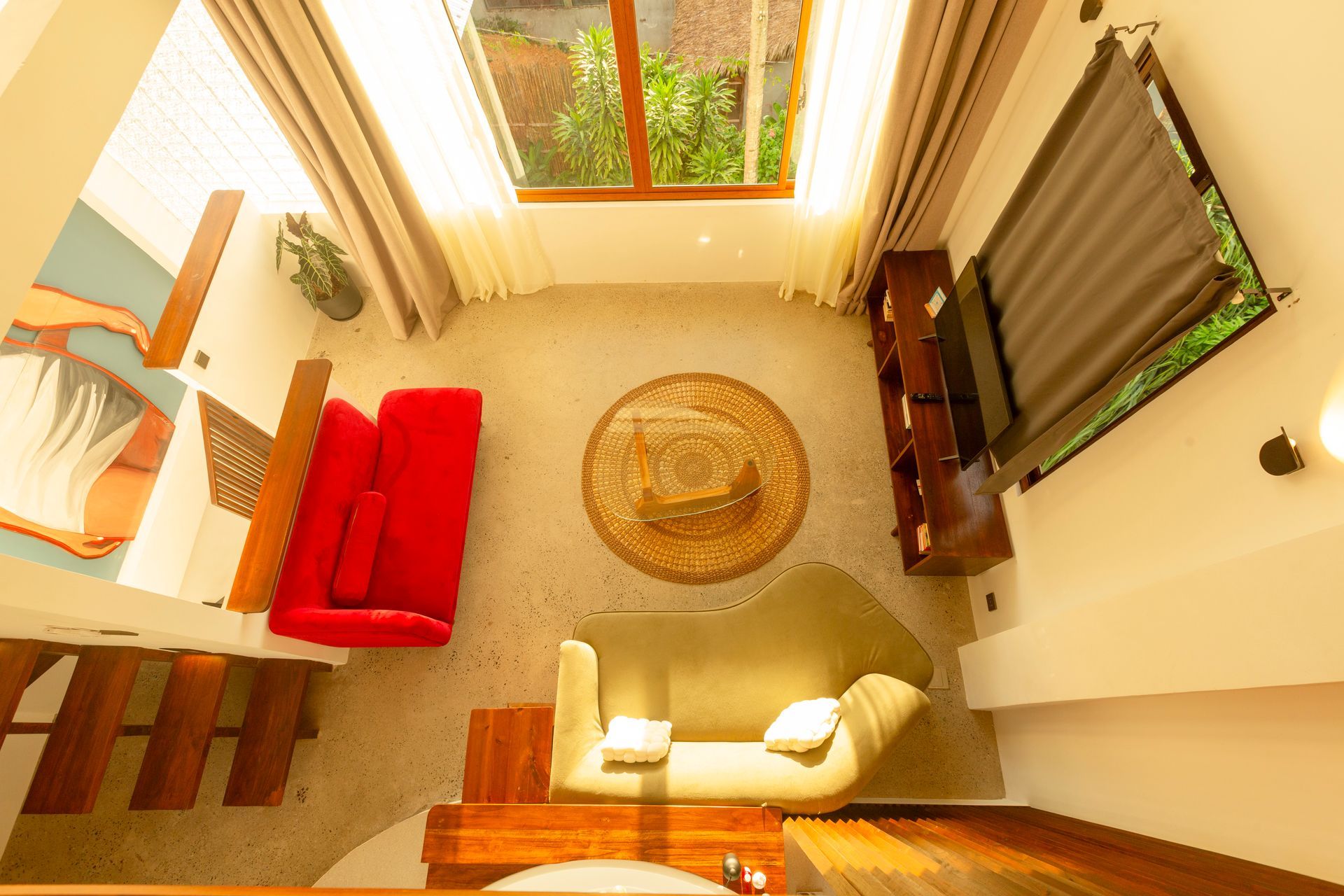 Overhead shot of a small living area. Red sofa, tan sofa, wooden shelves, and round table. Sunlight streams in from a window.
