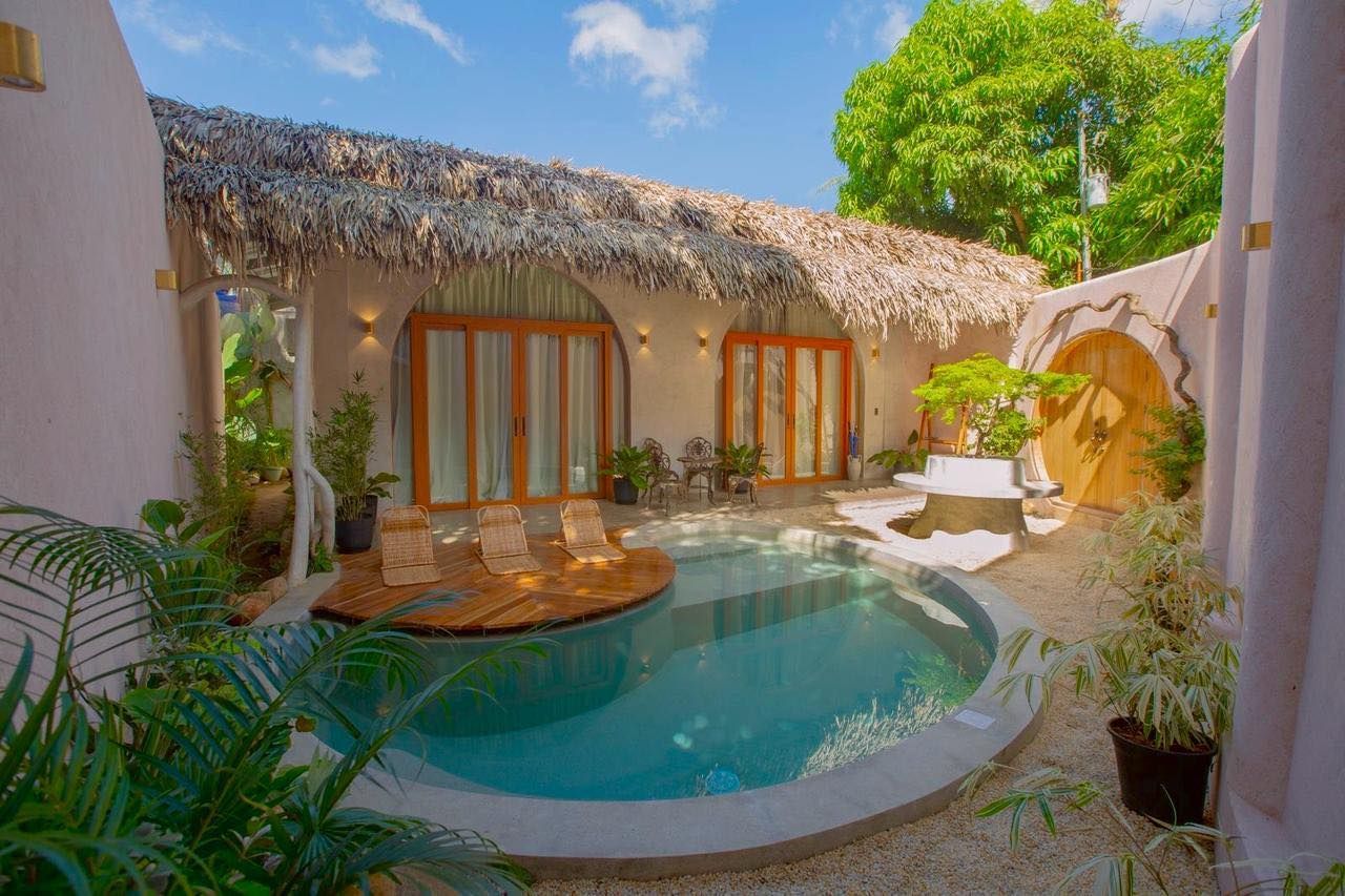 Courtyard with small pool, thatched roof building, wooden deck, tropical plants.