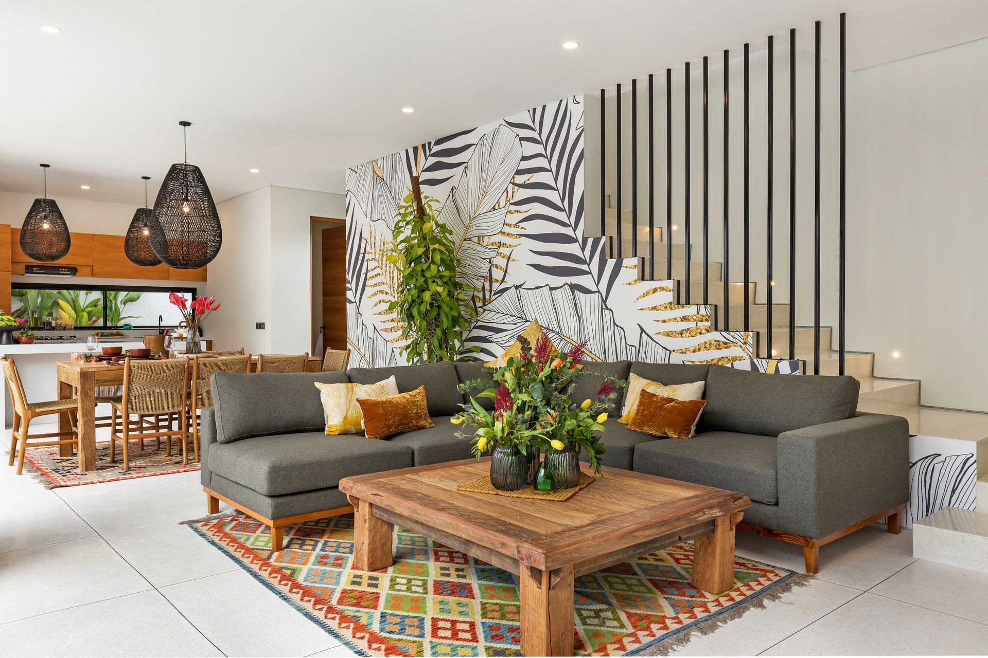 Living room with gray sectional sofa, wood coffee table, patterned rug, and tropical leaf wallpaper.