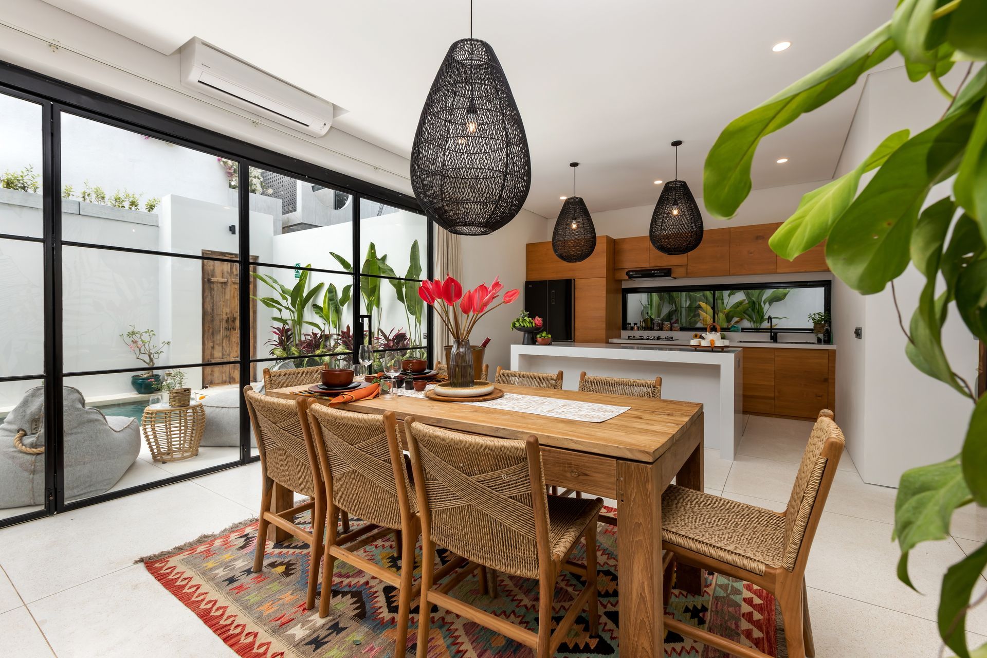 Dining room with wooden table and chairs, pendant lights, and view of a patio through a glass wall.