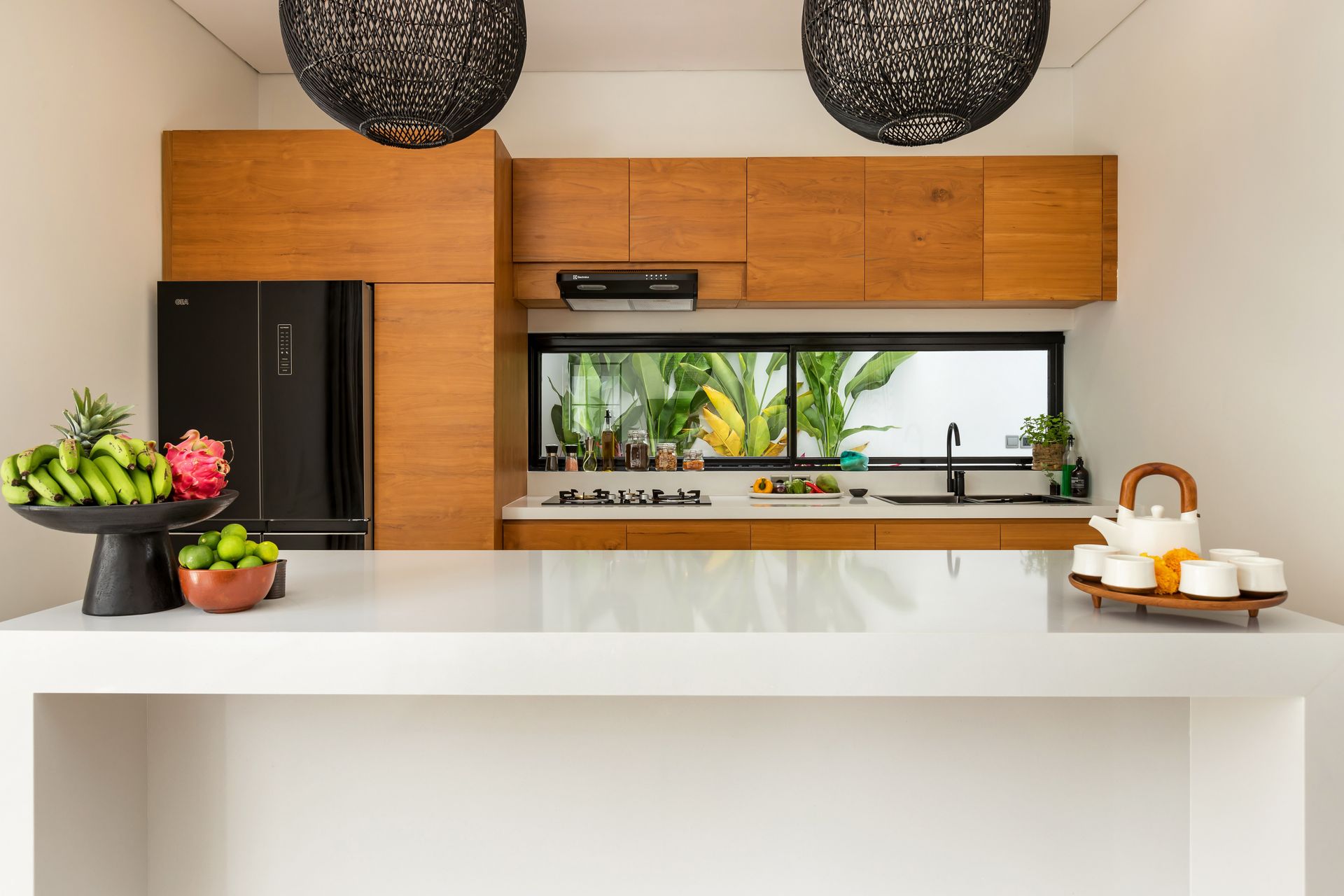 Kitchen with wooden cabinets, black refrigerator, white countertop, view of greenery through a window.
