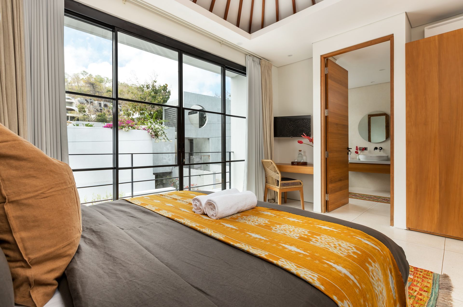 Bedroom with a large window, bed, desk, and open door to a bathroom.
