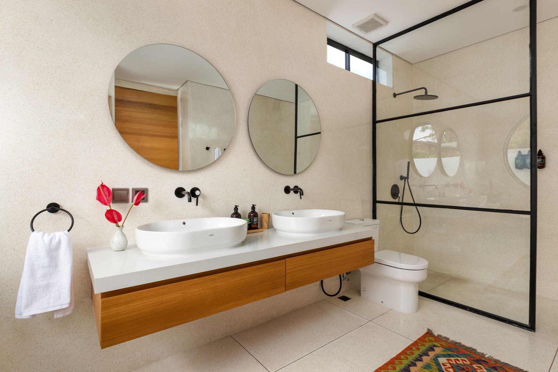 Modern bathroom with dual sinks, round mirrors, and glass-enclosed shower. Includes a white countertop and wooden cabinetry.