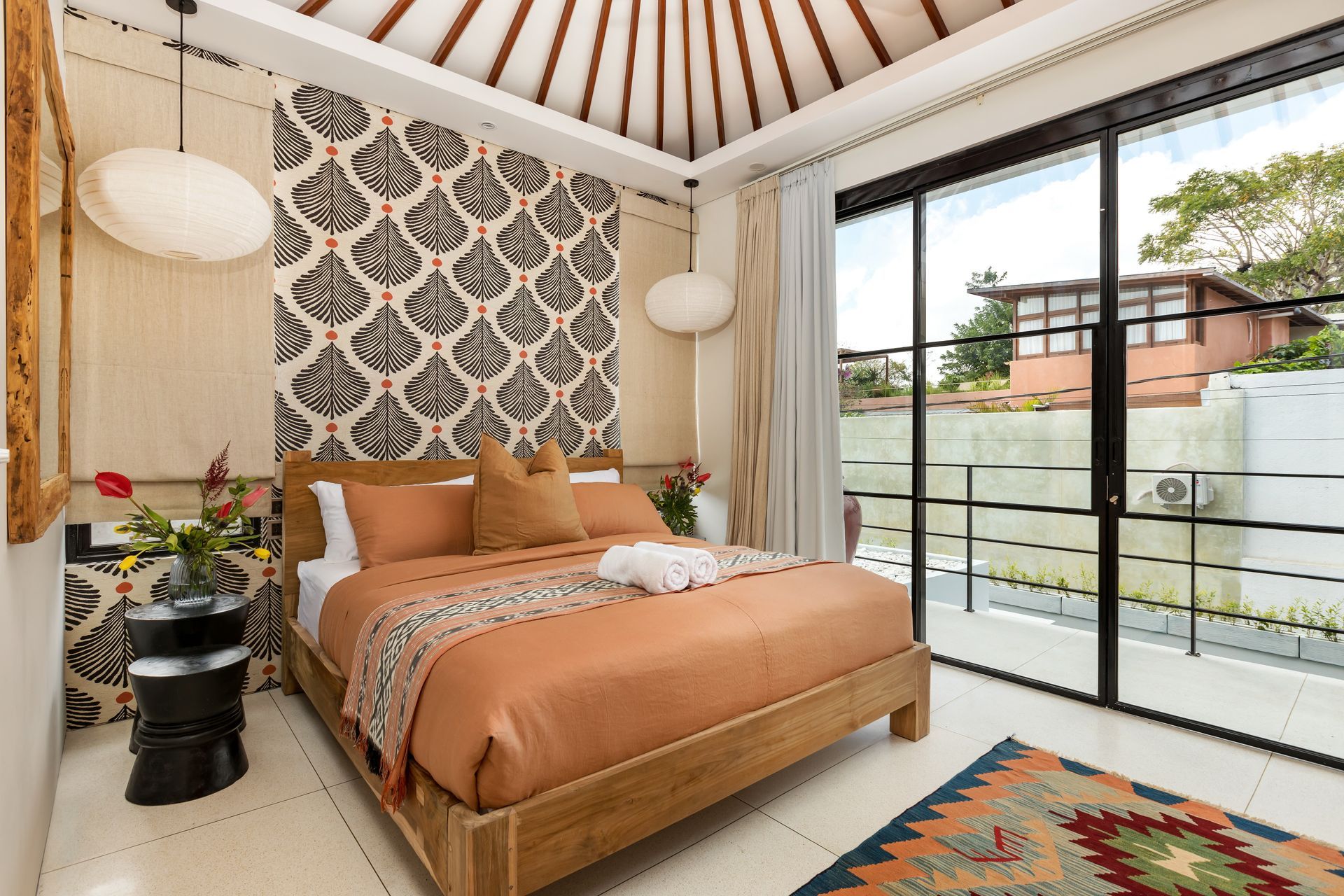 Bedroom with wood bed, patterned wallpaper, sliding glass doors, and patterned rug.