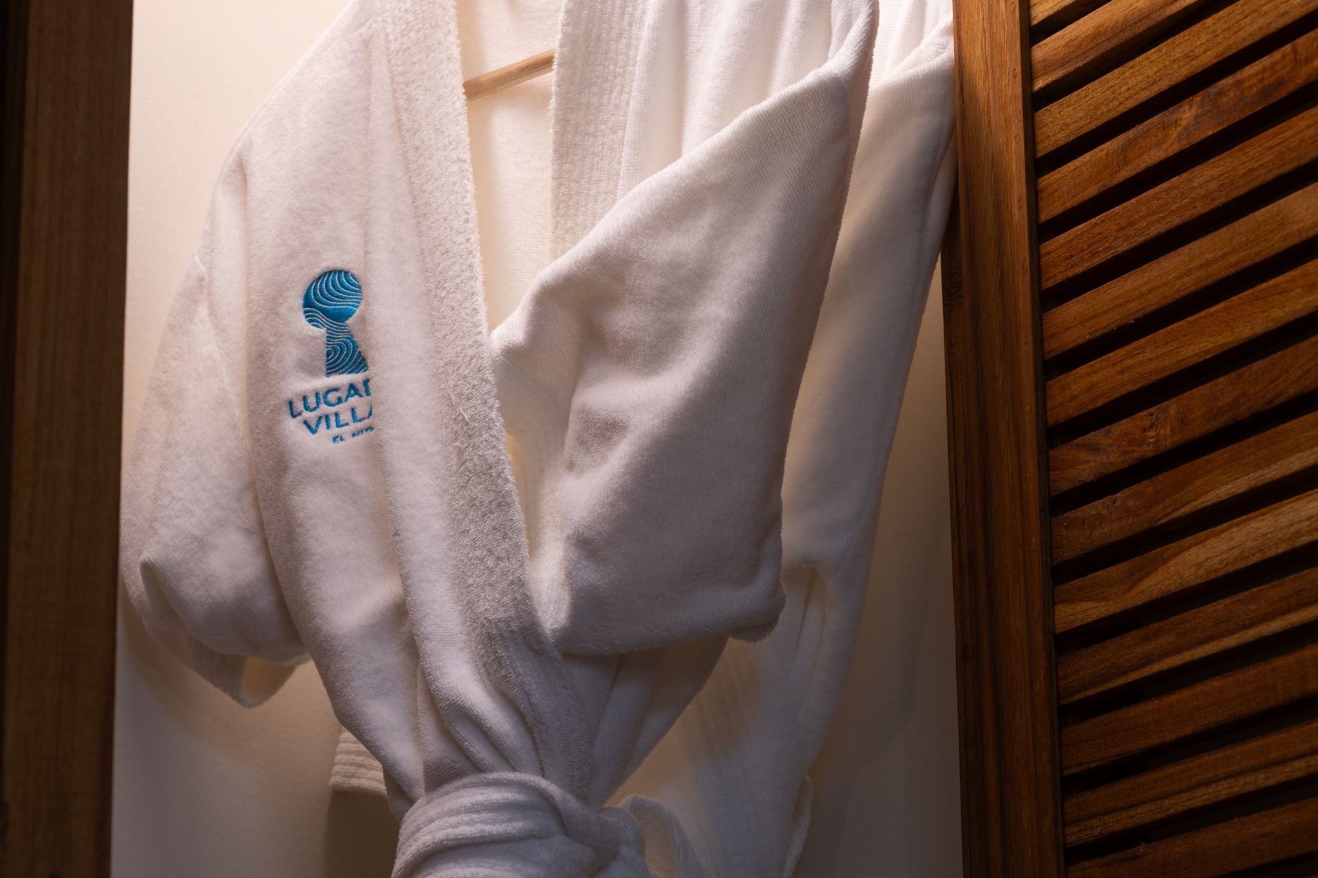 White bathrobe hanging in a wooden closet, with logo 
