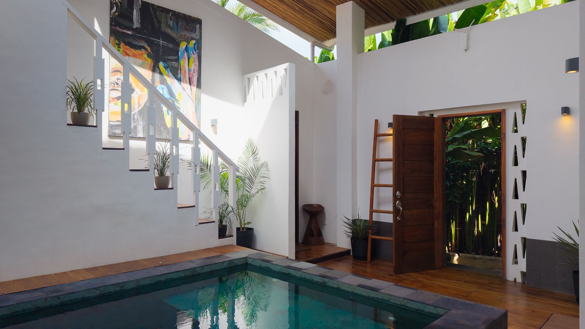 Indoor pool area with staircase, artwork, and open doorway to greenery.