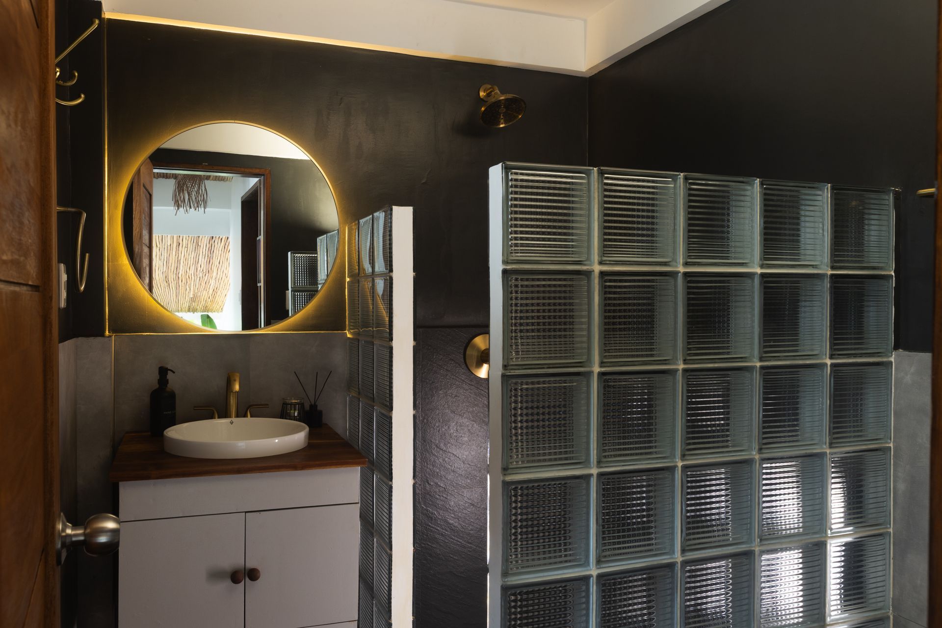 Bathroom with a round, lighted mirror, white sink, glass block shower wall, and dark gray walls.