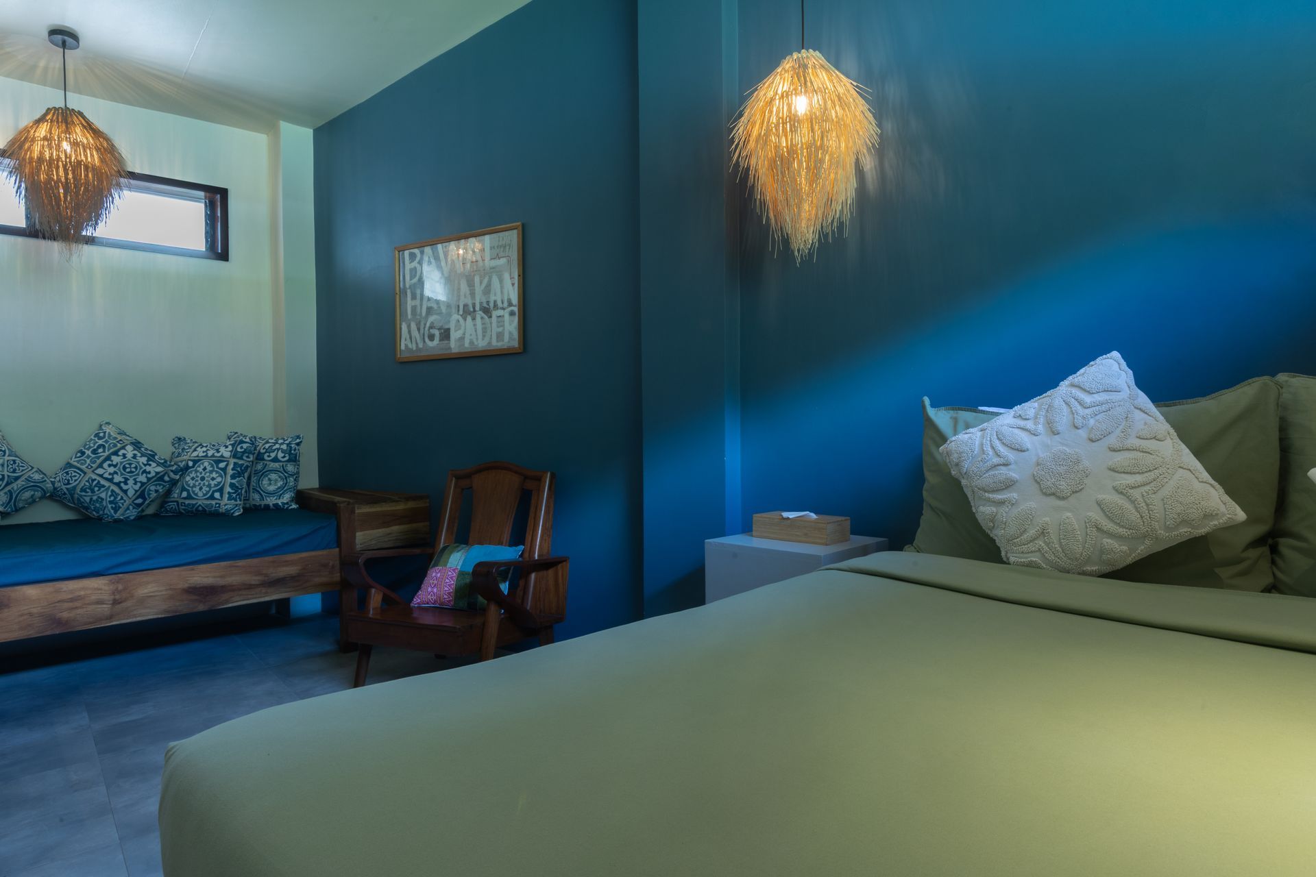Bedroom with blue walls, a bed, a wooden bench, and woven pendant lights.