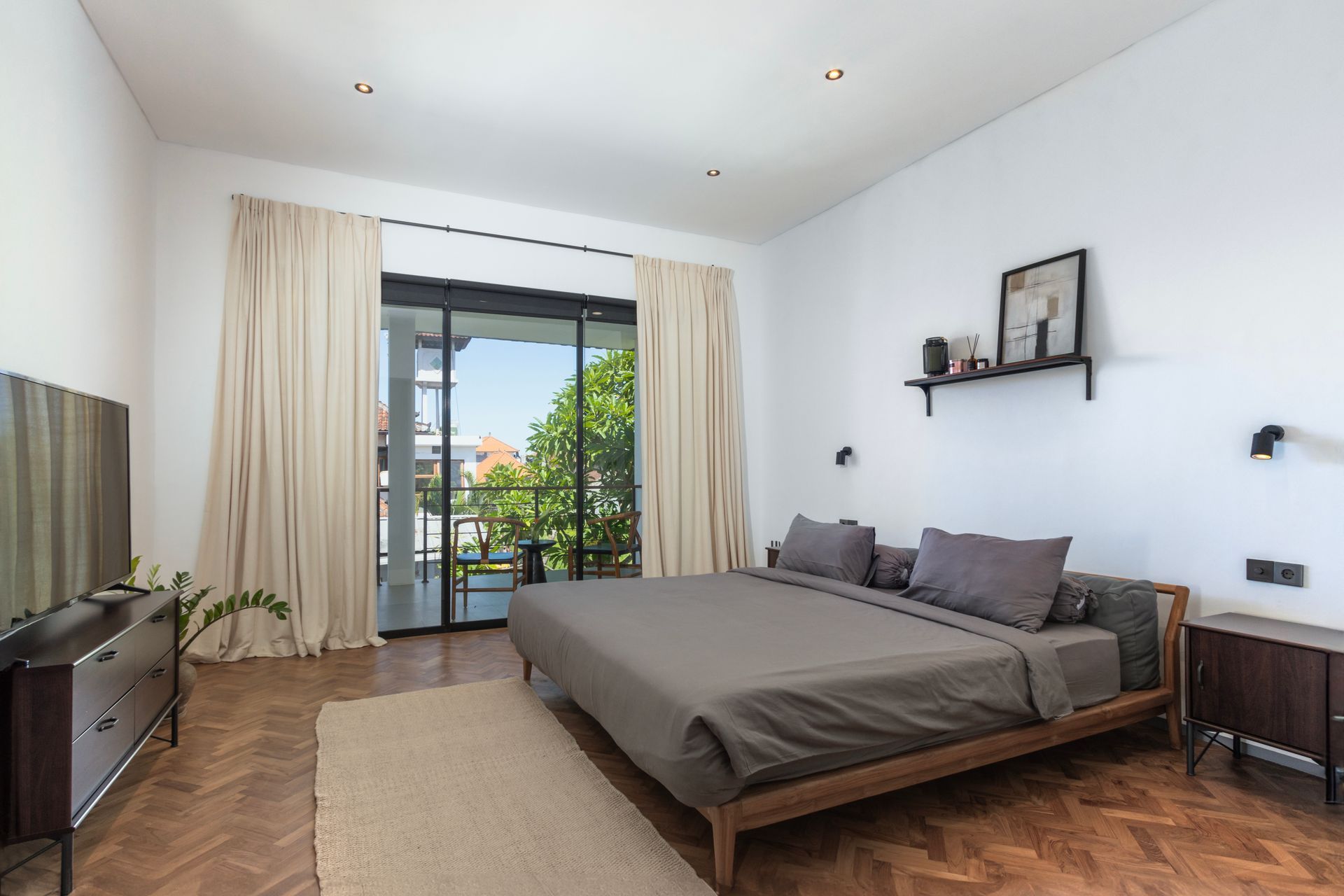 Bedroom with wooden bed frame, large window, and light-colored curtains. Dark dresser and nightstand present.