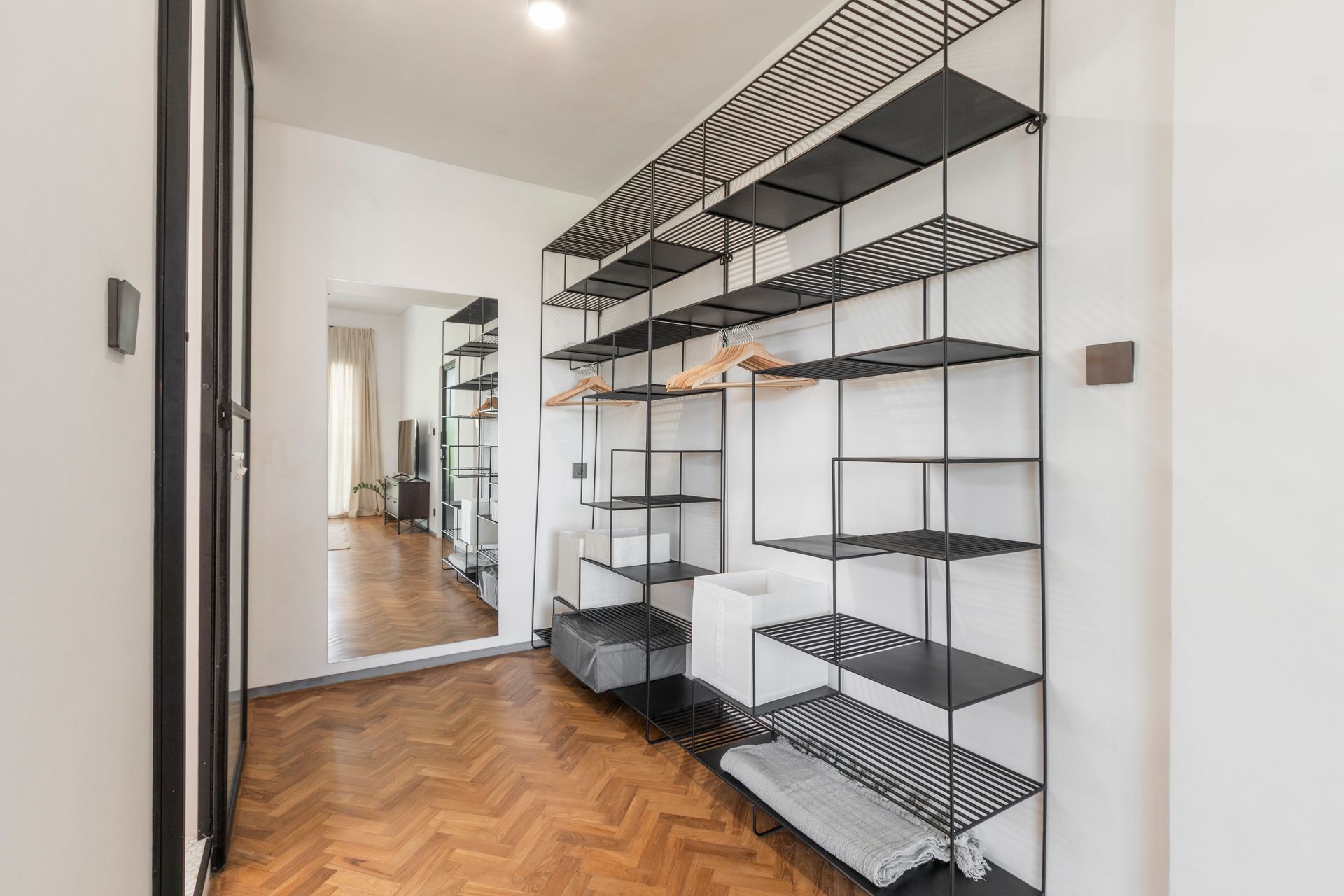 A modern hallway with black metal shelving against a white wall; herringbone wood floor.