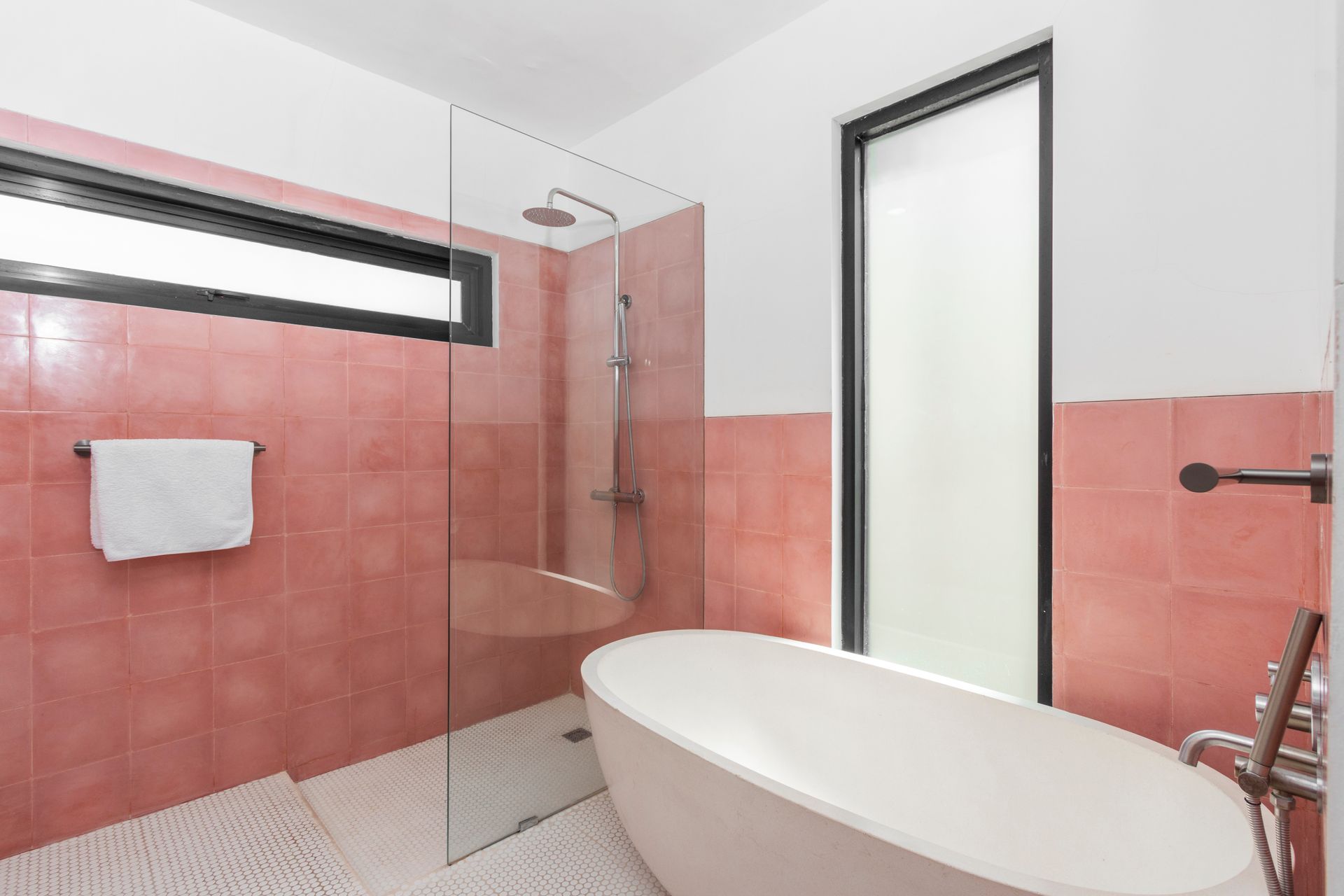 Bathroom with pink tiled walls, a white freestanding tub, and a glass shower.
